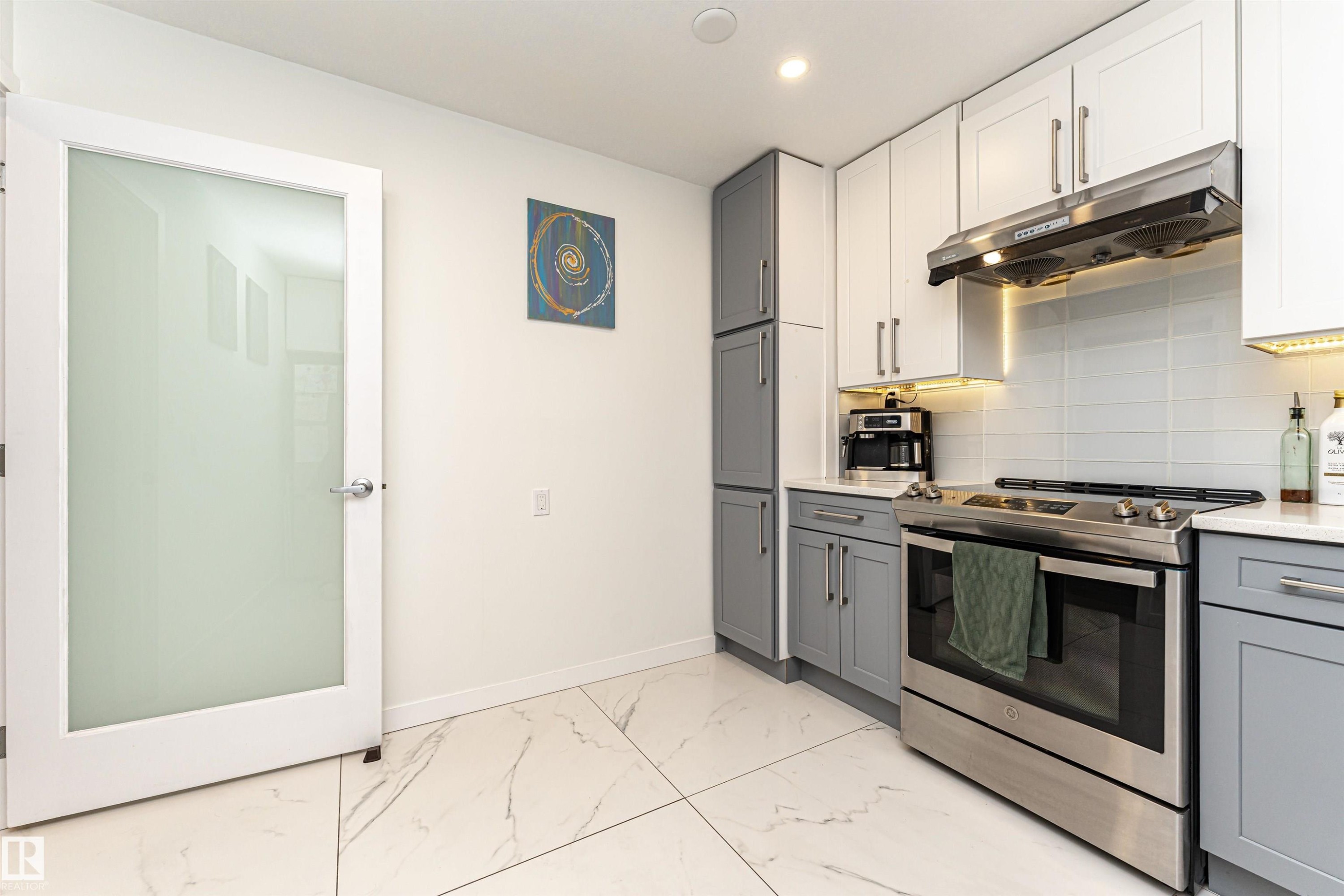 Kitchen featuring gray cabinetry, stainless steel range with gas stovetop, under cabinet range hood, tasteful backsplash, and light marble finish floors - 17716 84 Avenue, Edmonton, AB - Indoor Photo Showing Kitchen With Upgraded Kitchen