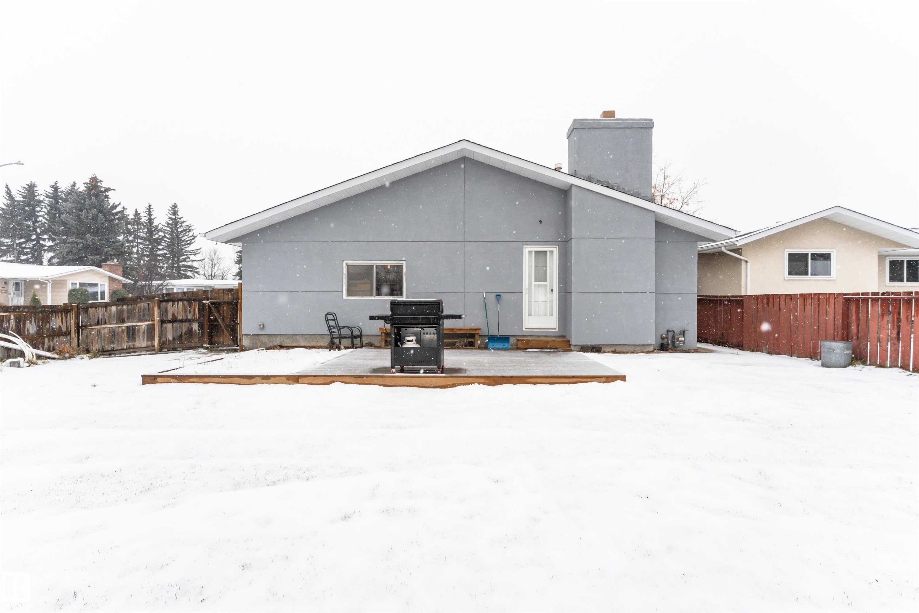 Snow covered back of property with a fenced backyard, a chimney, stucco siding, and a patio - 17716 84 Avenue, Edmonton, AB - Outdoor