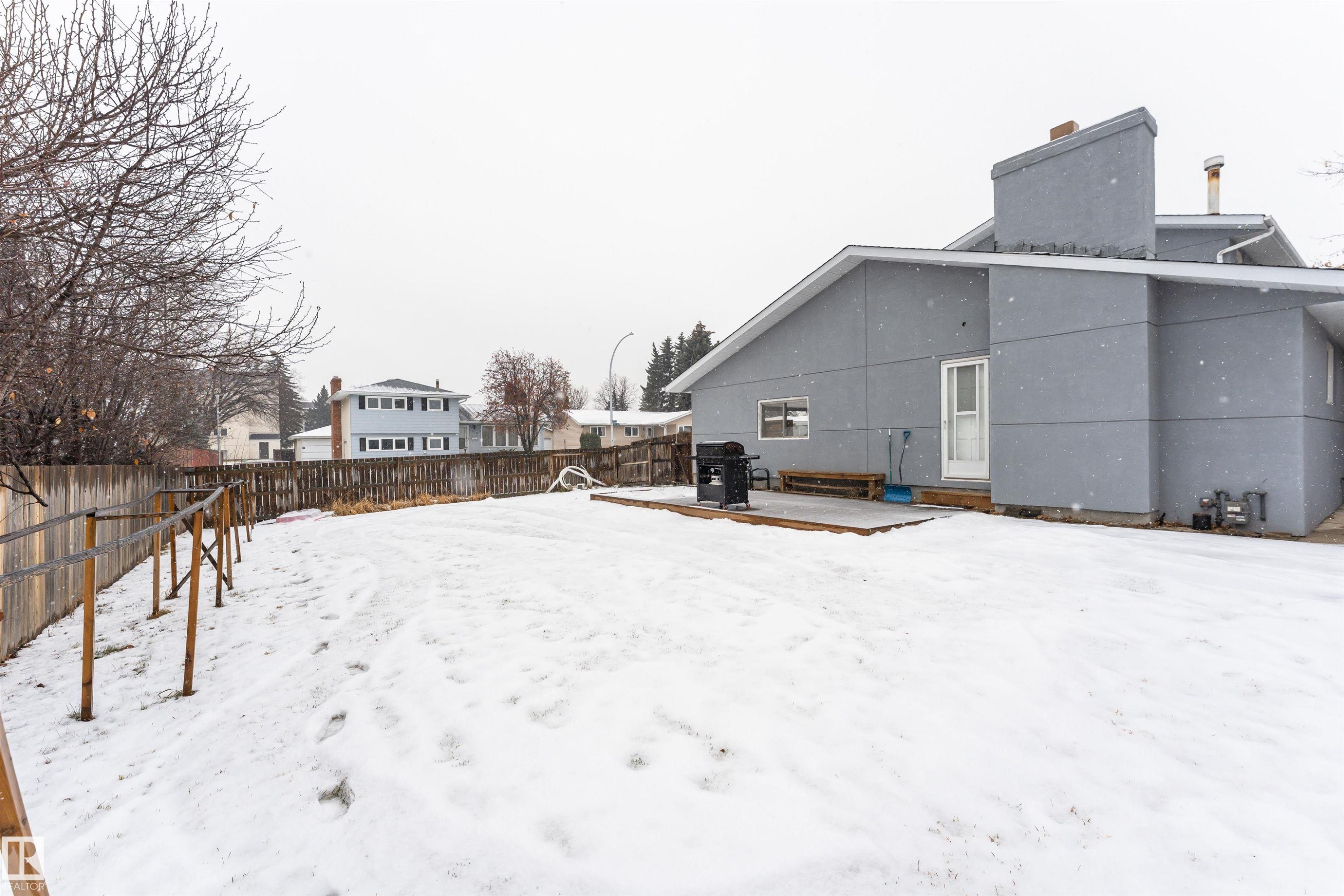 Snow covered rear of property featuring a fenced backyard, a chimney, a wooden deck, and a patio area - 17716 84 Avenue, Edmonton, AB - Outdoor