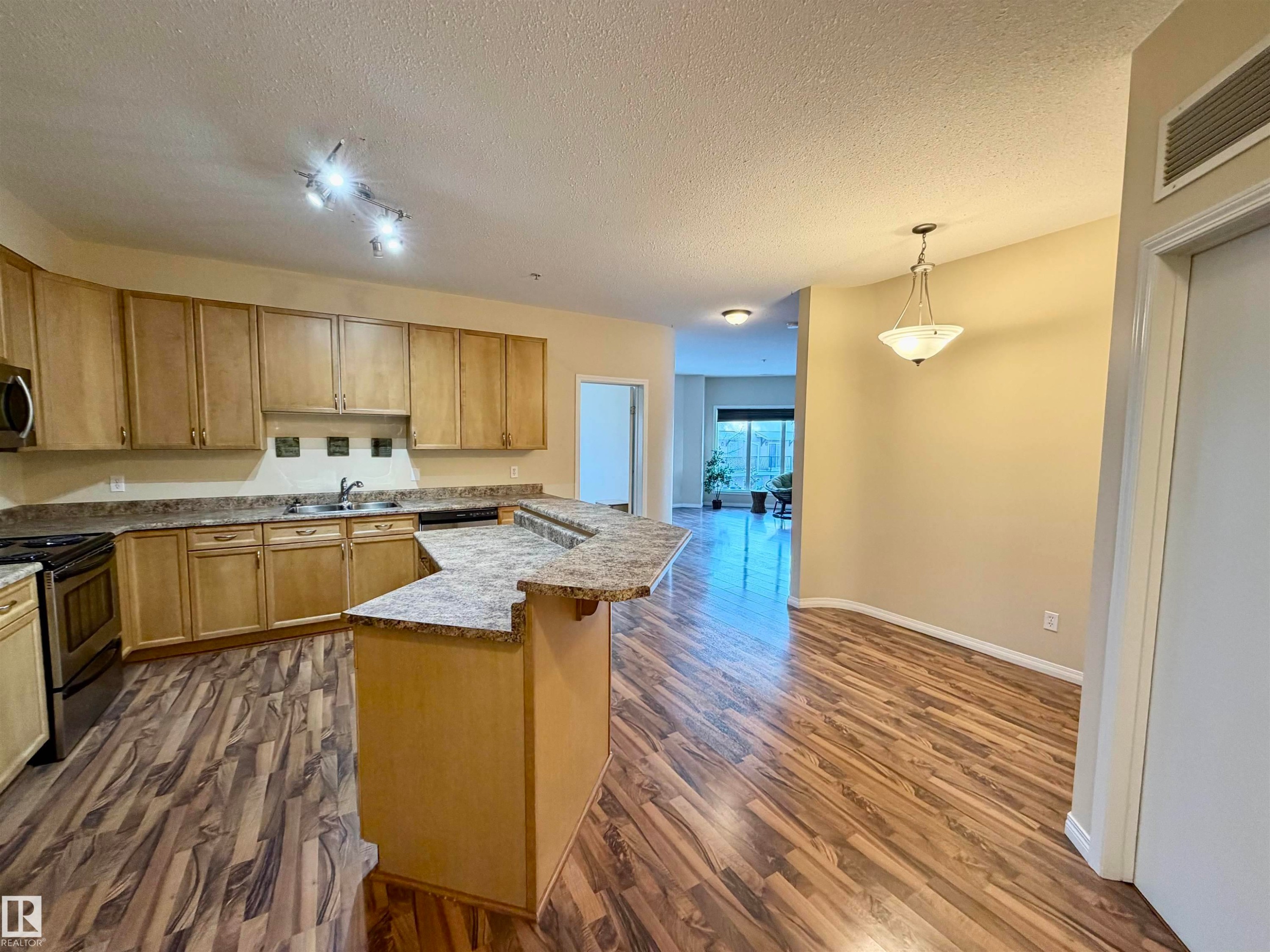 Kitchen with stainless steel appliances, dark wood-style flooring, decorative light fixtures, a textured ceiling, and a kitchen island - 321 4304 139 Avenue, Edmonton, AB - Indoor Photo Showing Kitchen With Double Sink