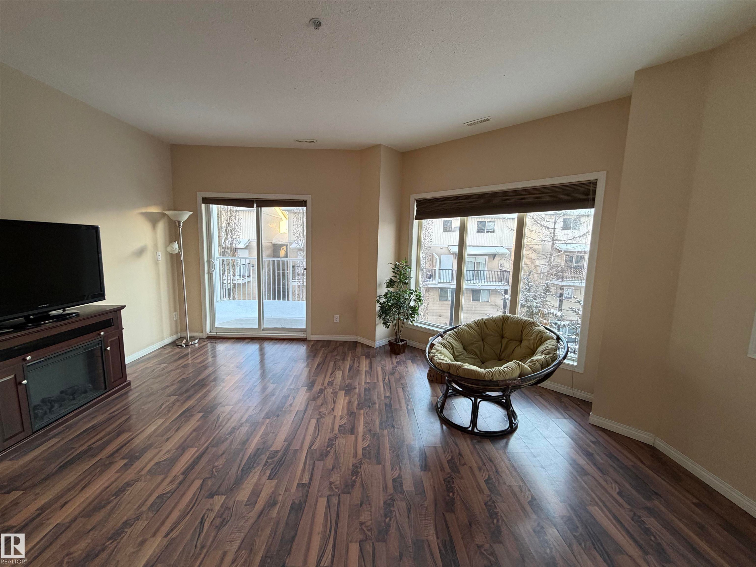 Sitting room with dark wood-style floors, a glass covered fireplace, and healthy amount of natural light - 321 4304 139 Avenue, Edmonton, AB - Indoor Photo Showing Other Room