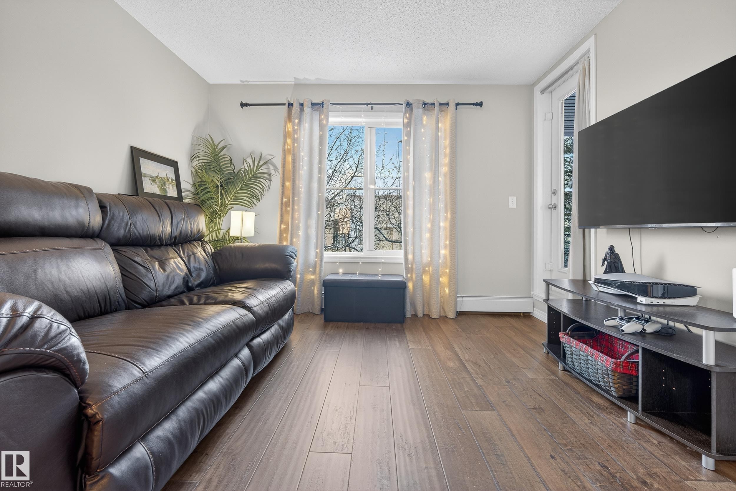 Living room featuring a textured ceiling, wood-type flooring, and a baseboard heating unit - 108 534 Watt Boulevard, Edmonton, AB - Indoor Photo Showing Living Room