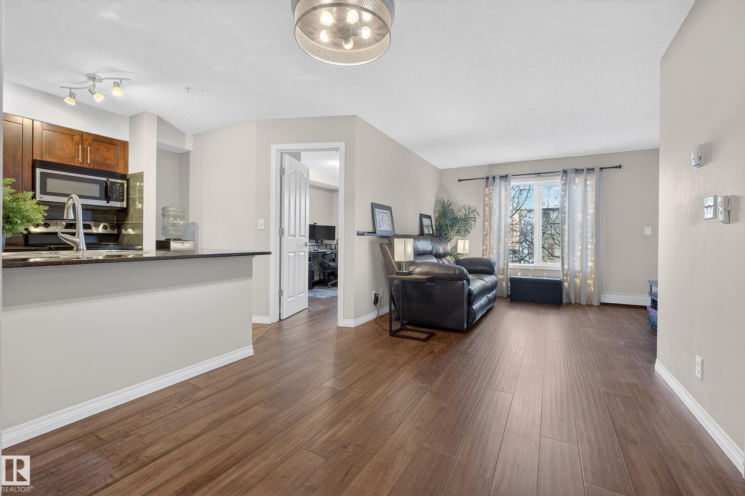 Living room featuring dark wood-style floors and baseboards - 108 534 Watt Boulevard, Edmonton, AB - Indoor