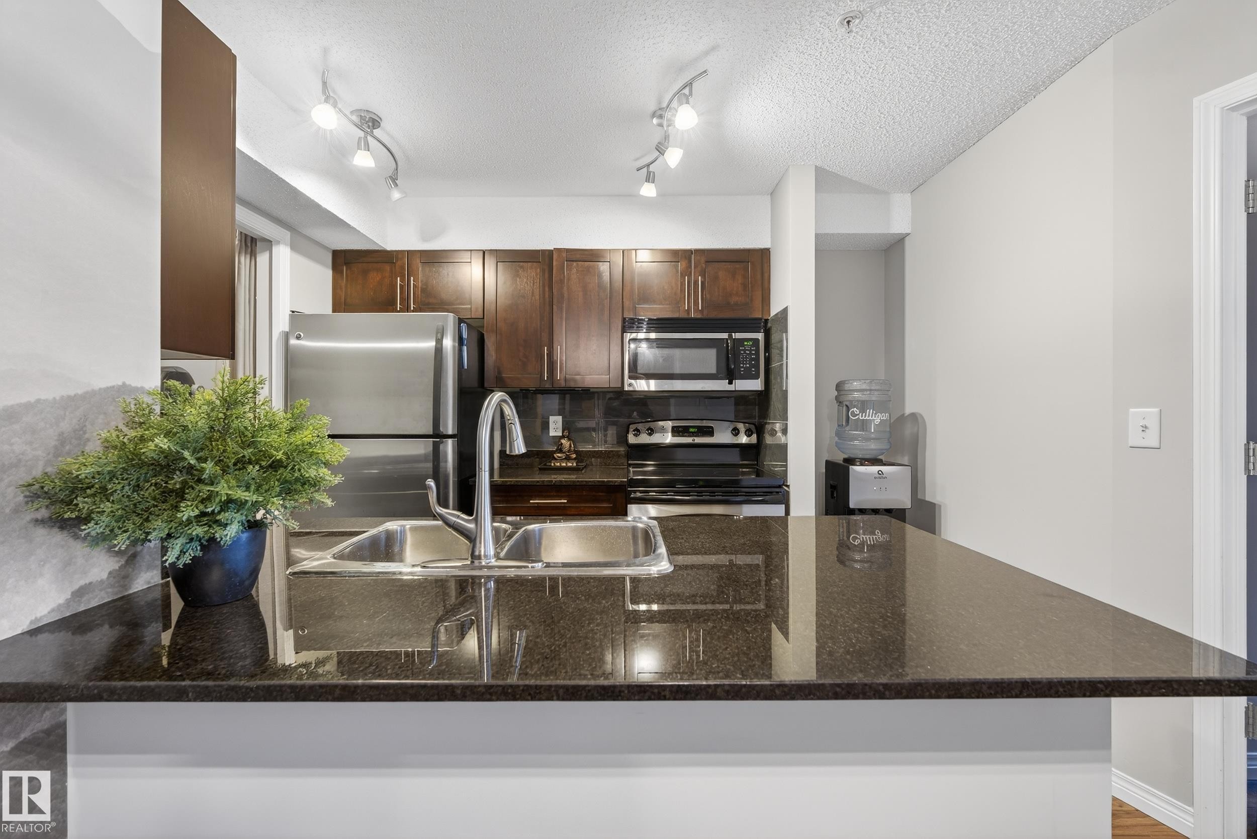 Kitchen featuring stainless steel appliances, dark stone countertops, decorative backsplash, a peninsula, and a textured ceiling - 108 534 Watt Boulevard, Edmonton, AB - Indoor Photo Showing Kitchen With Double Sink