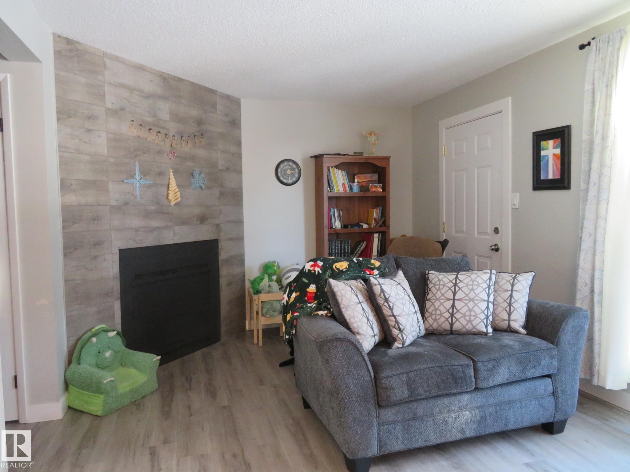 Living area featuring wood finished floors, a fireplace, an accent wall, and a textured ceiling - 3103 109 Street, Edmonton, AB - Indoor Photo Showing Living Room With Fireplace