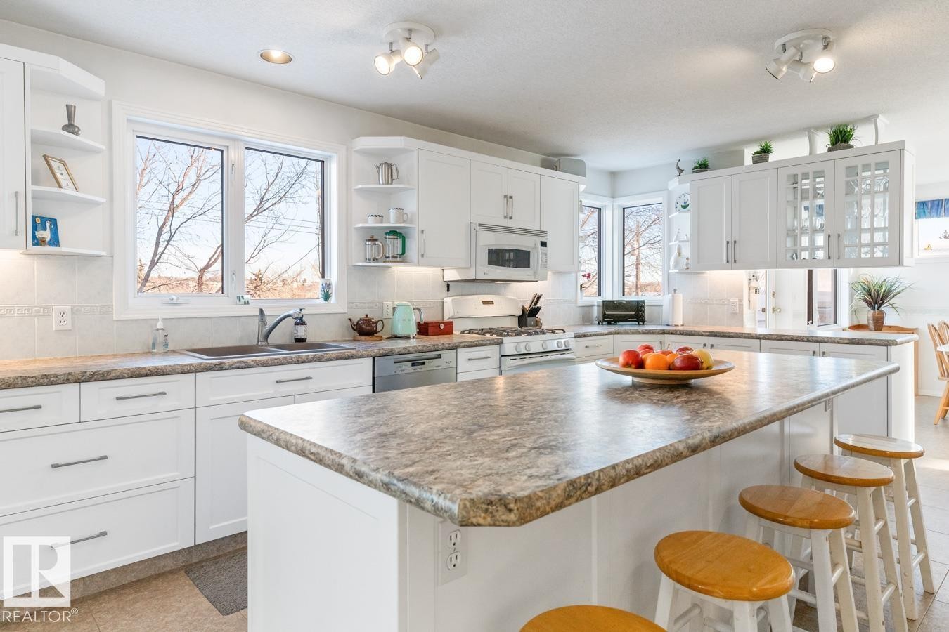 Kitchen with white cabinets, a kitchen breakfast bar, a center island, white appliances, and open shelves - 6508 109 Avenue, Edmonton, AB - Indoor Photo Showing Kitchen With Double Sink