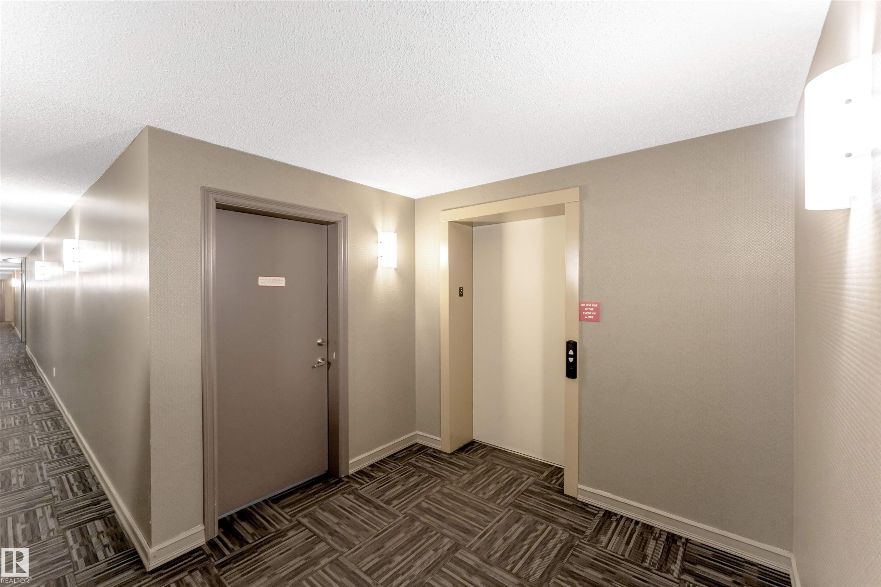 Hall with elevator, dark colored carpet, and a textured ceiling - #201 4403 23 Street Nw, Edmonton, AB - Indoor Photo Showing Other Room