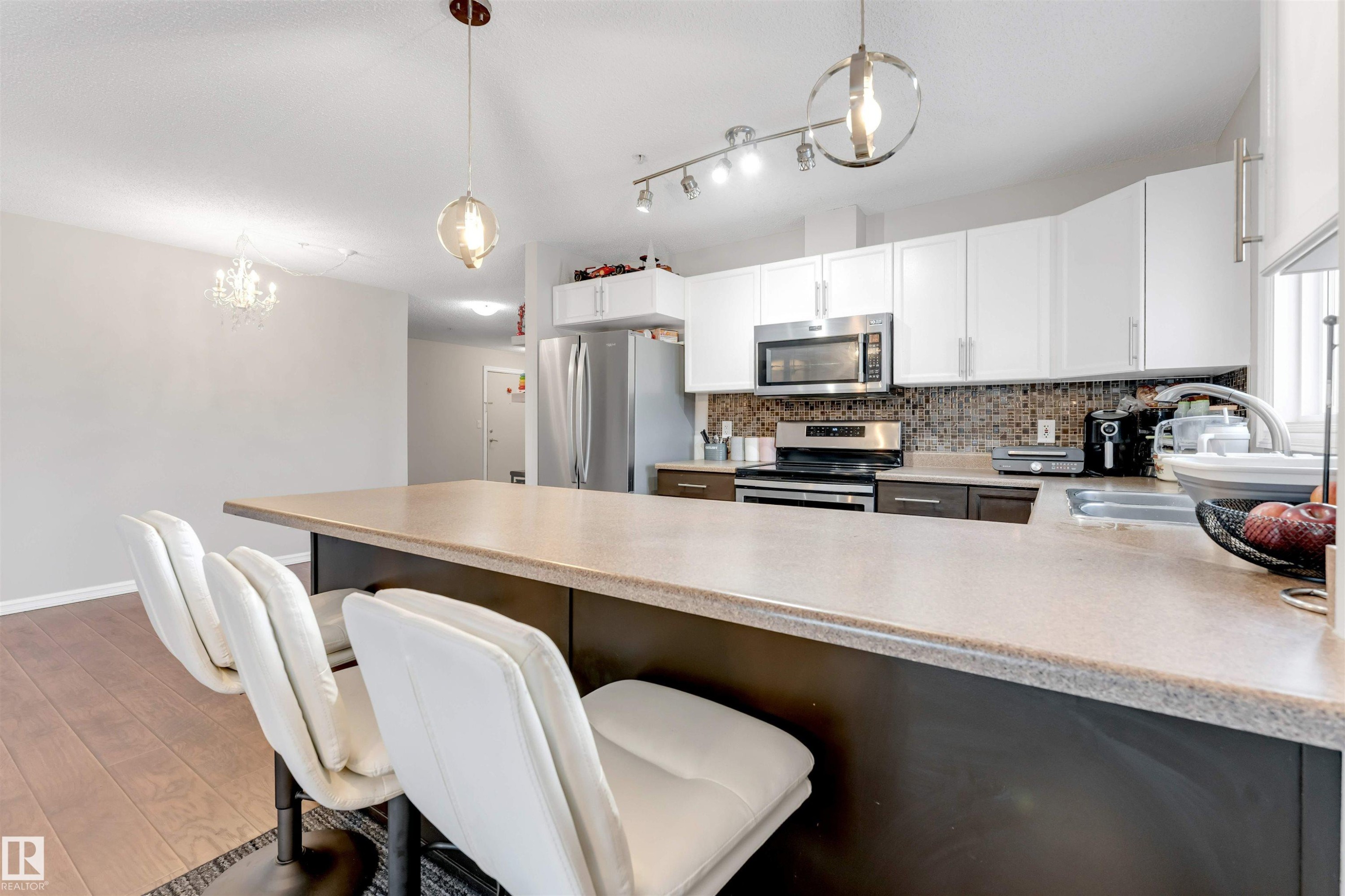 Kitchen featuring a kitchen breakfast bar, appliances with stainless steel finishes, a peninsula, hanging light fixtures, and tasteful backsplash - #201 4403 23 Street Nw, Edmonton, AB - Indoor Photo Showing Kitchen With Stainless Steel Kitchen With Double Sink With Upgraded Kitchen