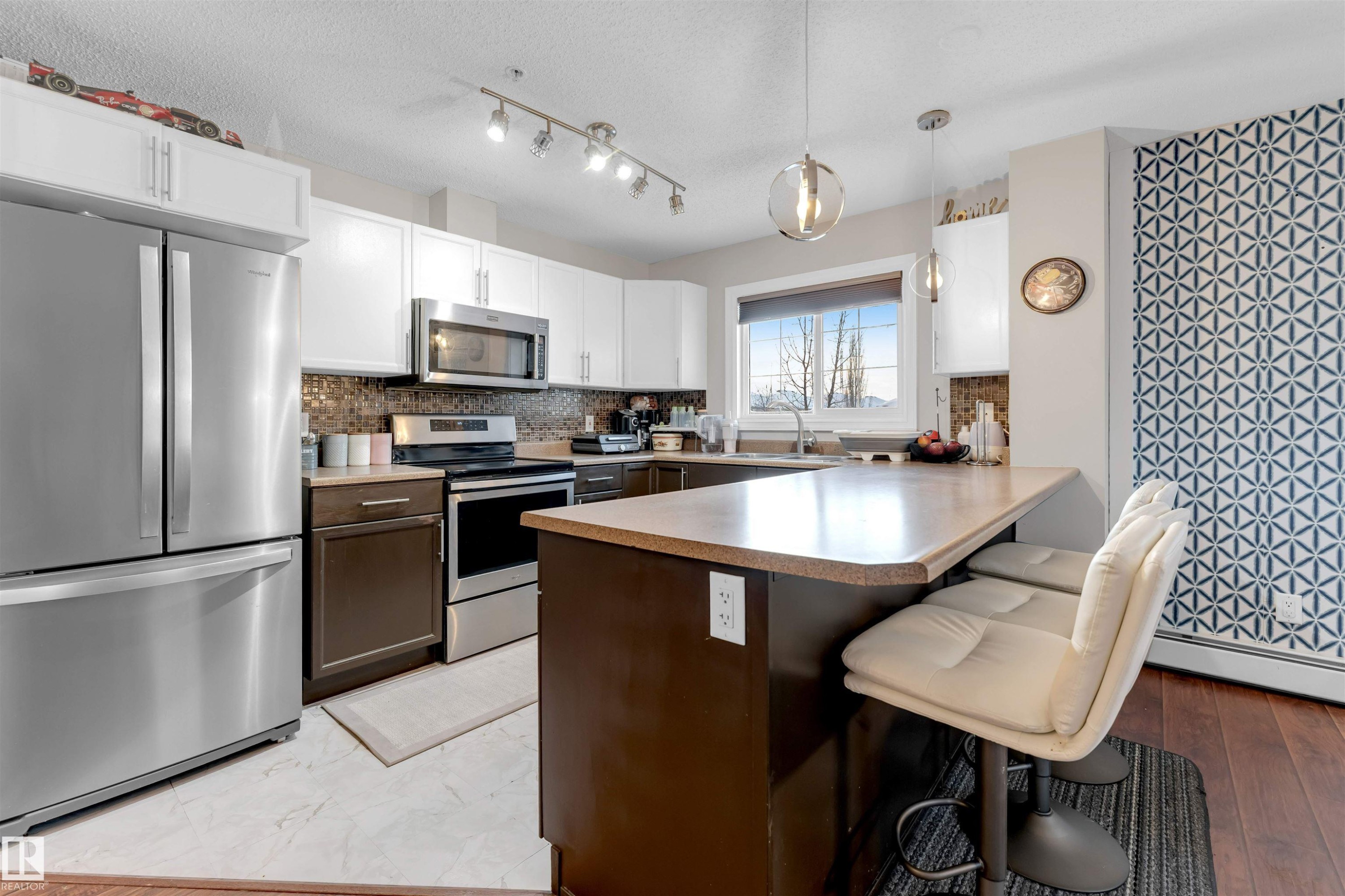 Kitchen with appliances with stainless steel finishes, a peninsula, a kitchen breakfast bar, light countertops, and white cabinets - #201 4403 23 Street Nw, Edmonton, AB - Indoor Photo Showing Kitchen With Stainless Steel Kitchen