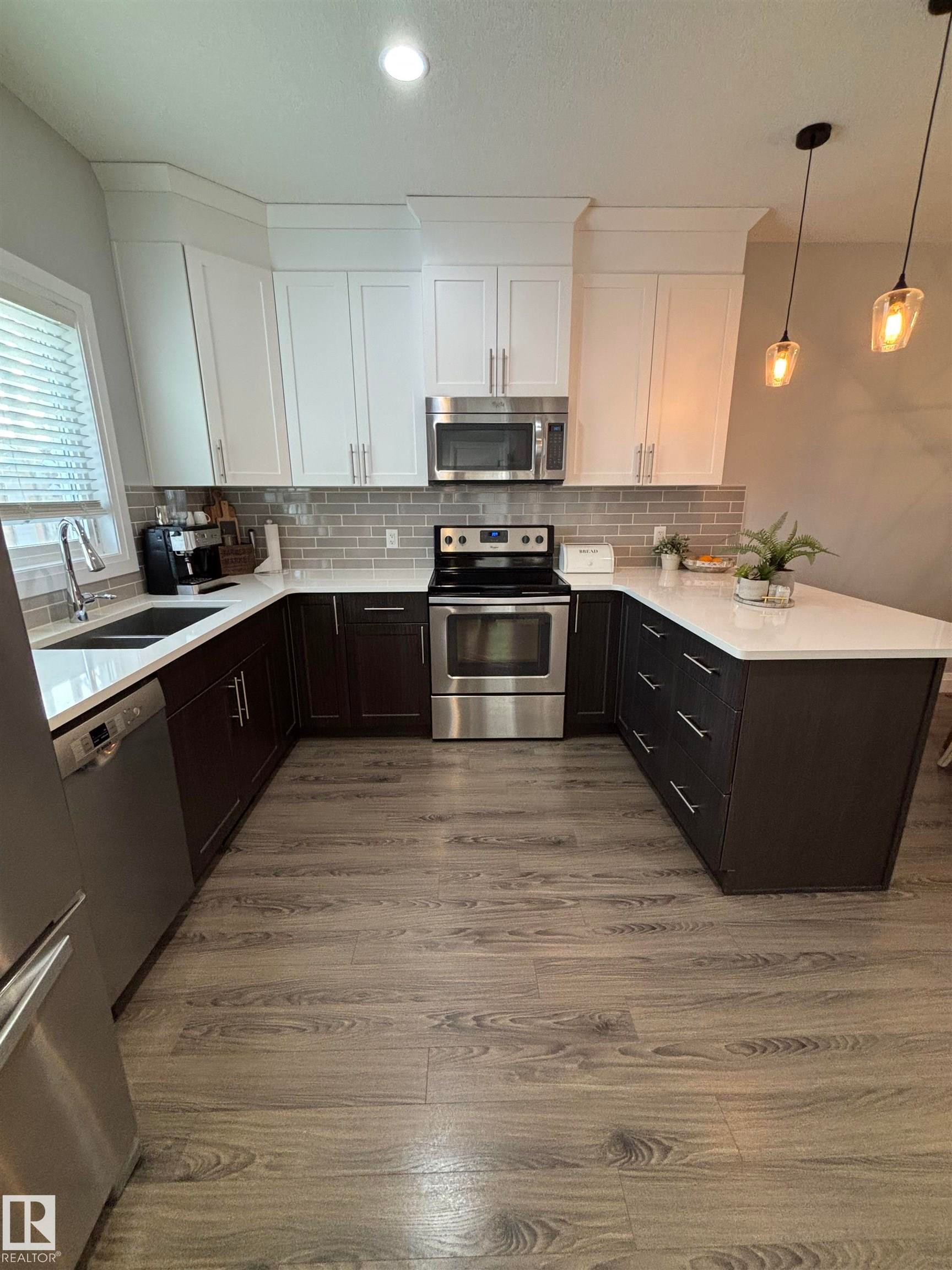Kitchen featuring white cabinets, appliances with stainless steel finishes, pendant lighting, and light stone counters - 25 Harrison Gate, Spruce Grove, AB - Indoor Photo Showing Kitchen With Double Sink With Upgraded Kitchen