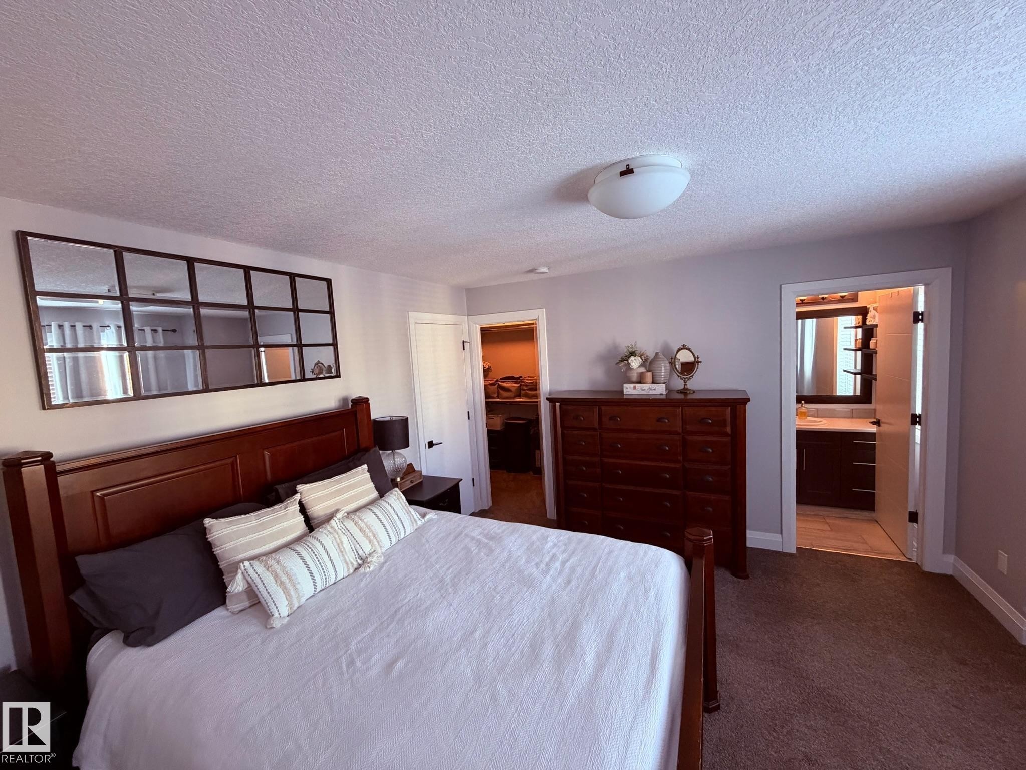 Bedroom featuring a textured ceiling, dark carpet, a walk in closet, and ensuite bathroom - 25 Harrison Gate, Spruce Grove, AB - Indoor Photo Showing Bedroom