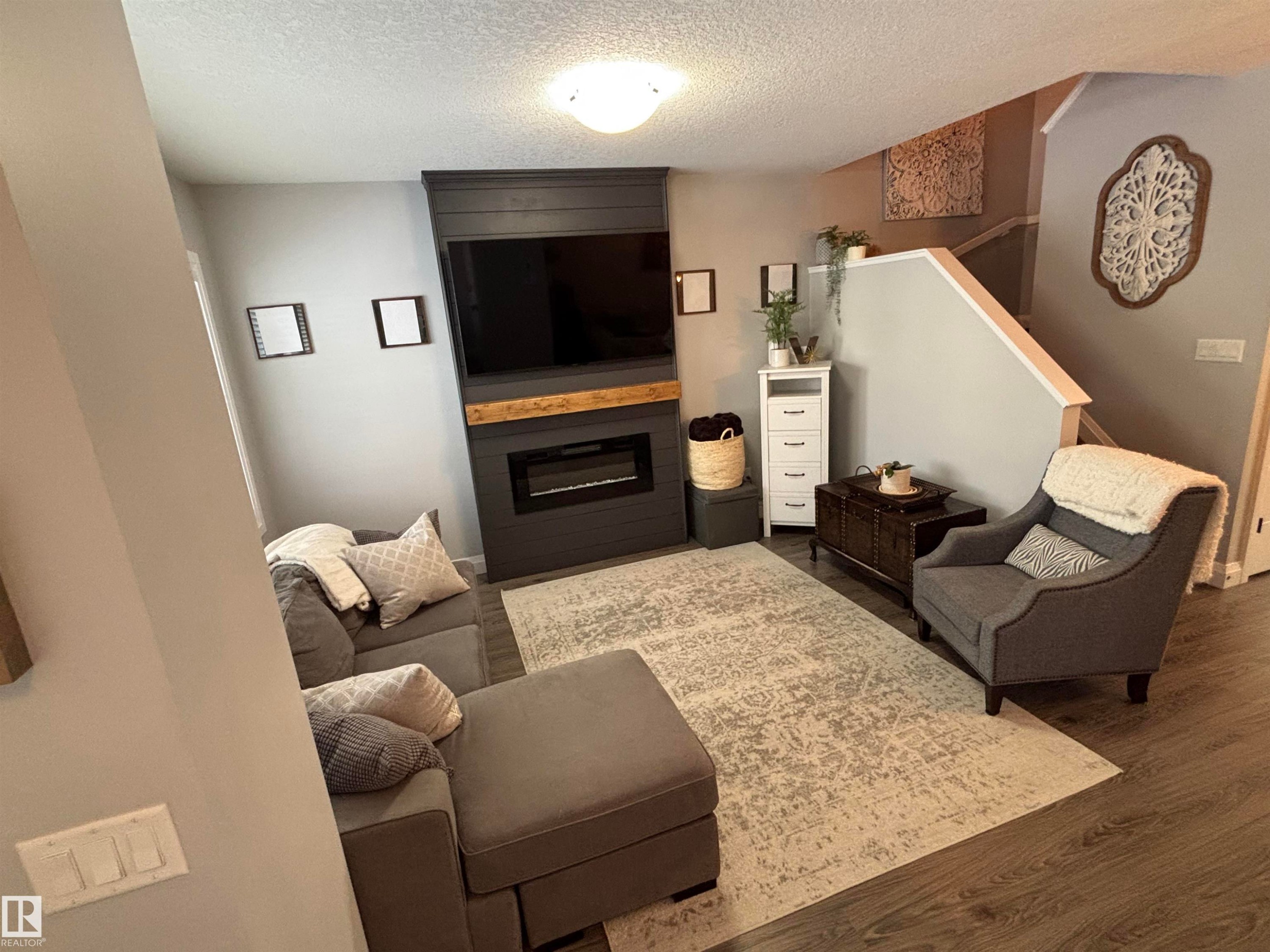 Living area featuring dark wood-style floors, a large fireplace, and a textured ceiling - 25 Harrison Gate, Spruce Grove, AB - Indoor With Fireplace