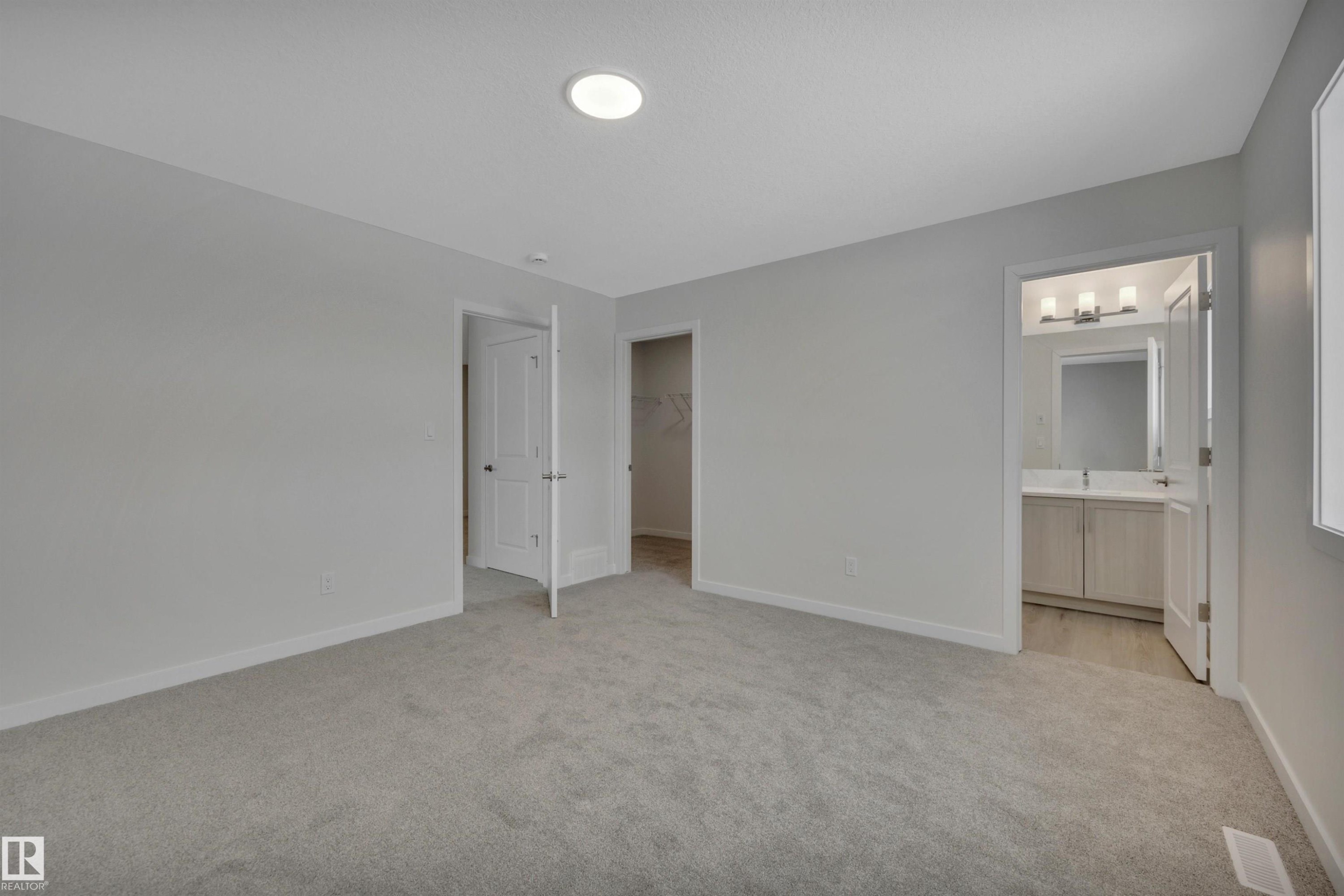 Unfurnished bedroom featuring a spacious closet, light colored carpet, and connected bathroom - 5742 Hawthorn Common, Edmonton, AB - Indoor