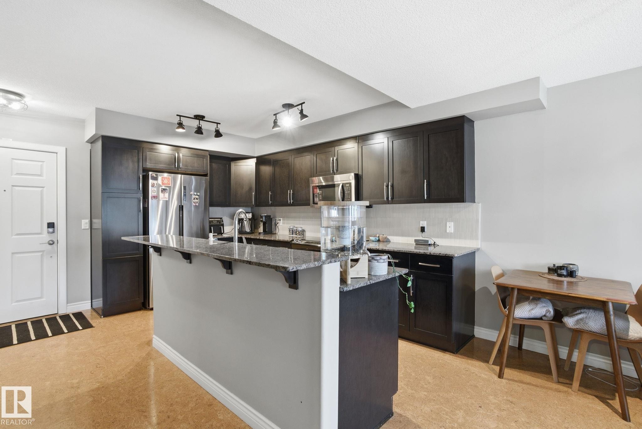 Kitchen featuring a breakfast bar area, tasteful backsplash, appliances with stainless steel finishes, dark stone countertops, and a kitchen island with sink - 301 9603 98 Avenue, Edmonton, AB - Indoor Photo Showing Kitchen With Upgraded Kitchen