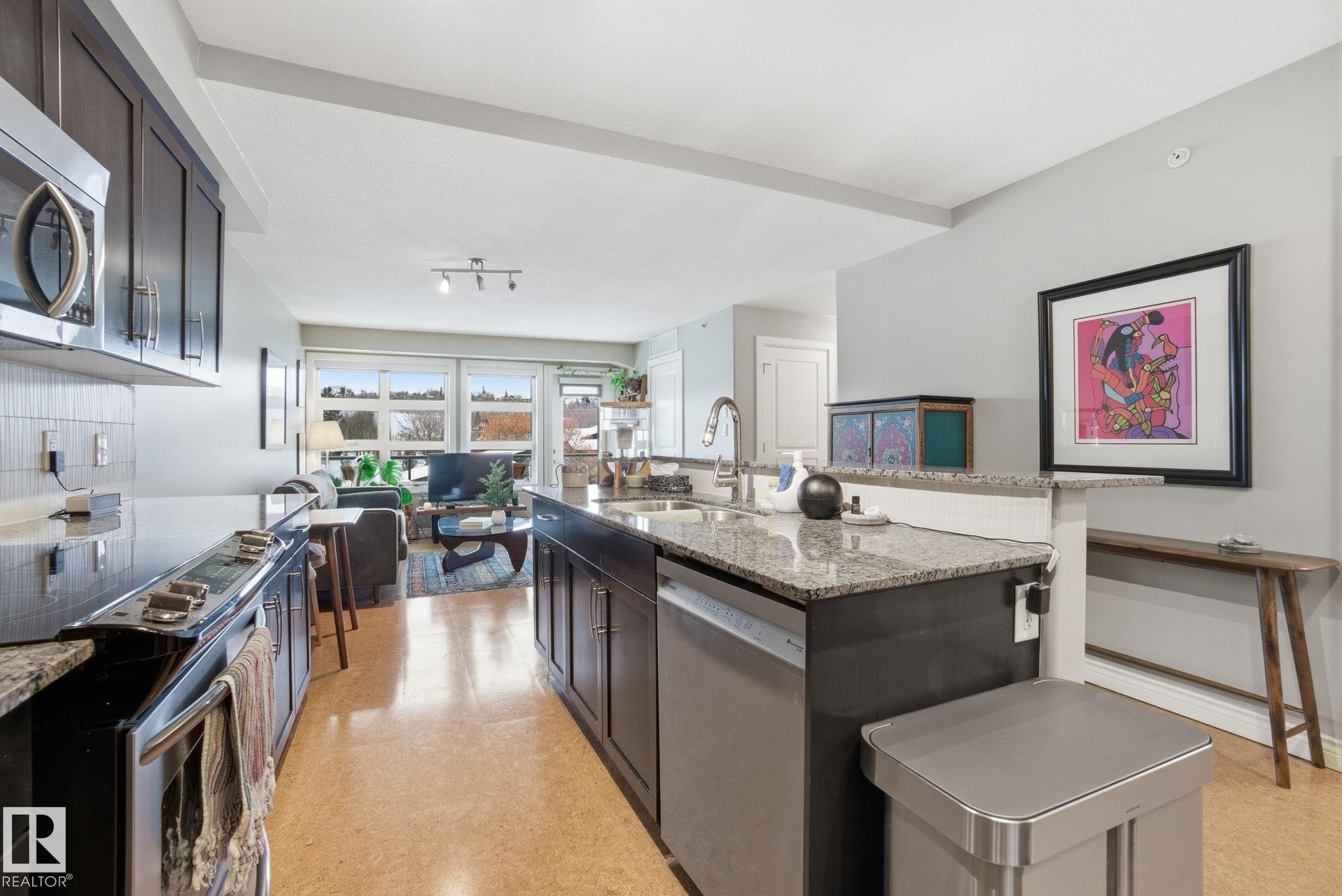 Kitchen featuring open floor plan, light stone counters, stainless steel appliances, and dark brown cabinetry - 301 9603 98 Avenue, Edmonton, AB - Indoor Photo Showing Kitchen With Upgraded Kitchen