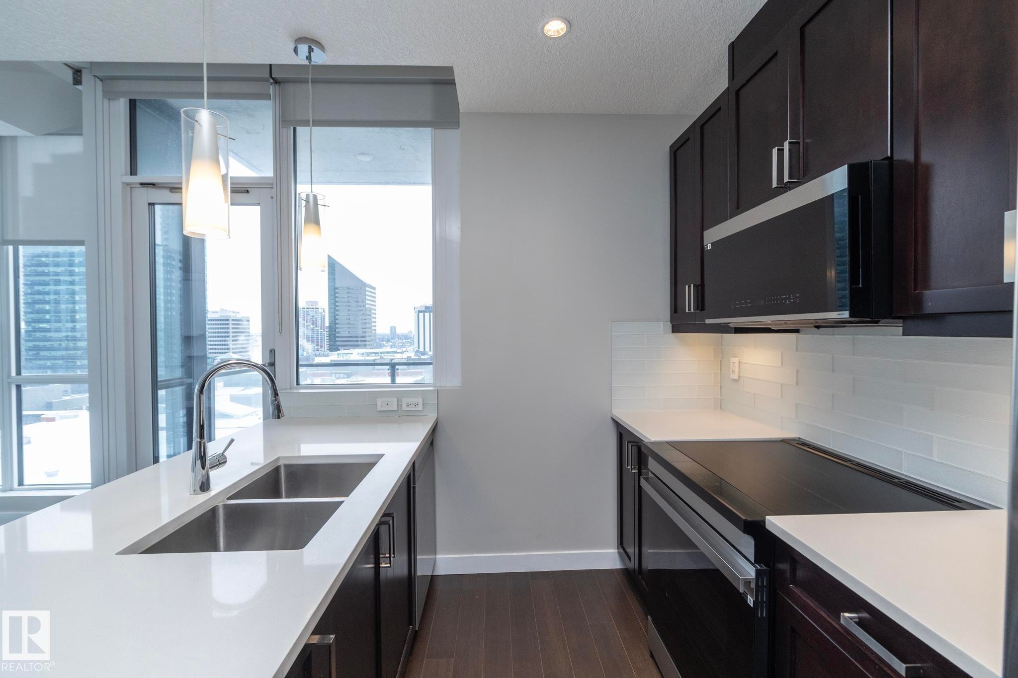 Kitchen with dark cabinetry, stainless steel electric range, decorative light fixtures, decorative backsplash, and light stone countertops - 1201 10238 103 Street, Edmonton, AB - Indoor Photo Showing Kitchen With Double Sink With Upgraded Kitchen