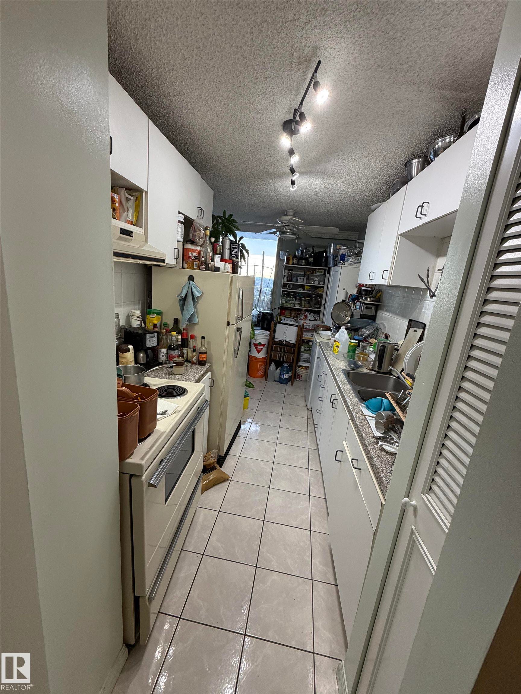 Kitchen featuring white cabinetry, light tile patterned flooring, white appliances, light countertops, and under cabinet range hood - 1506 10883 Saskatchewan Dr, Edmonton, AB - Indoor