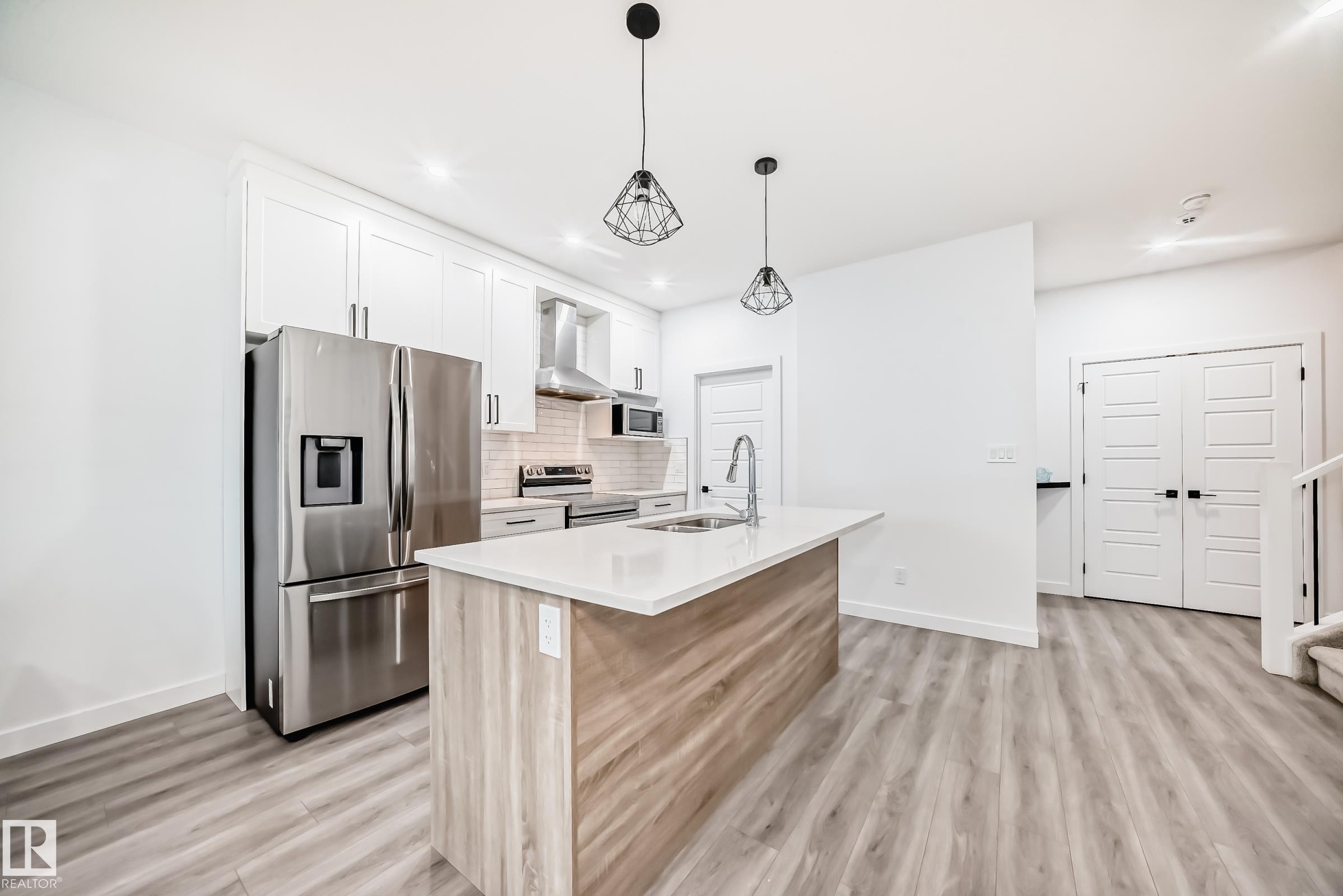 Kitchen with appliances with stainless steel finishes, white cabinets, a kitchen island with sink, wall chimney range hood, and recessed lighting - 563 Kleins Cr, Leduc, AB - Indoor Photo Showing Kitchen With Upgraded Kitchen