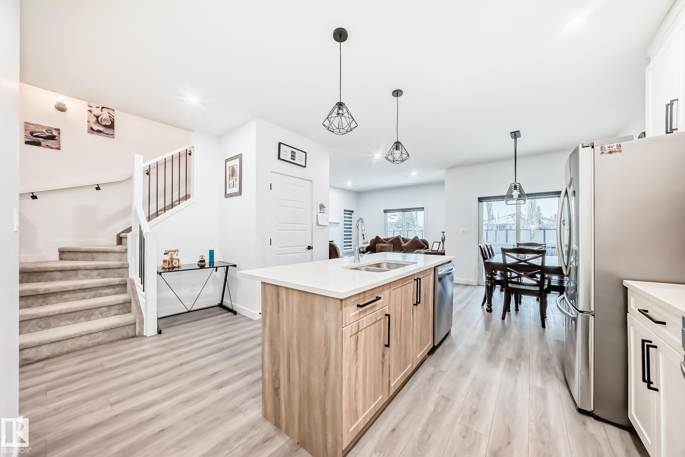 Kitchen with decorative light fixtures, stainless steel appliances, a center island with sink, light brown cabinetry, and open floor plan - 563 Kleins Cr, Leduc, AB - Indoor Photo Showing Kitchen