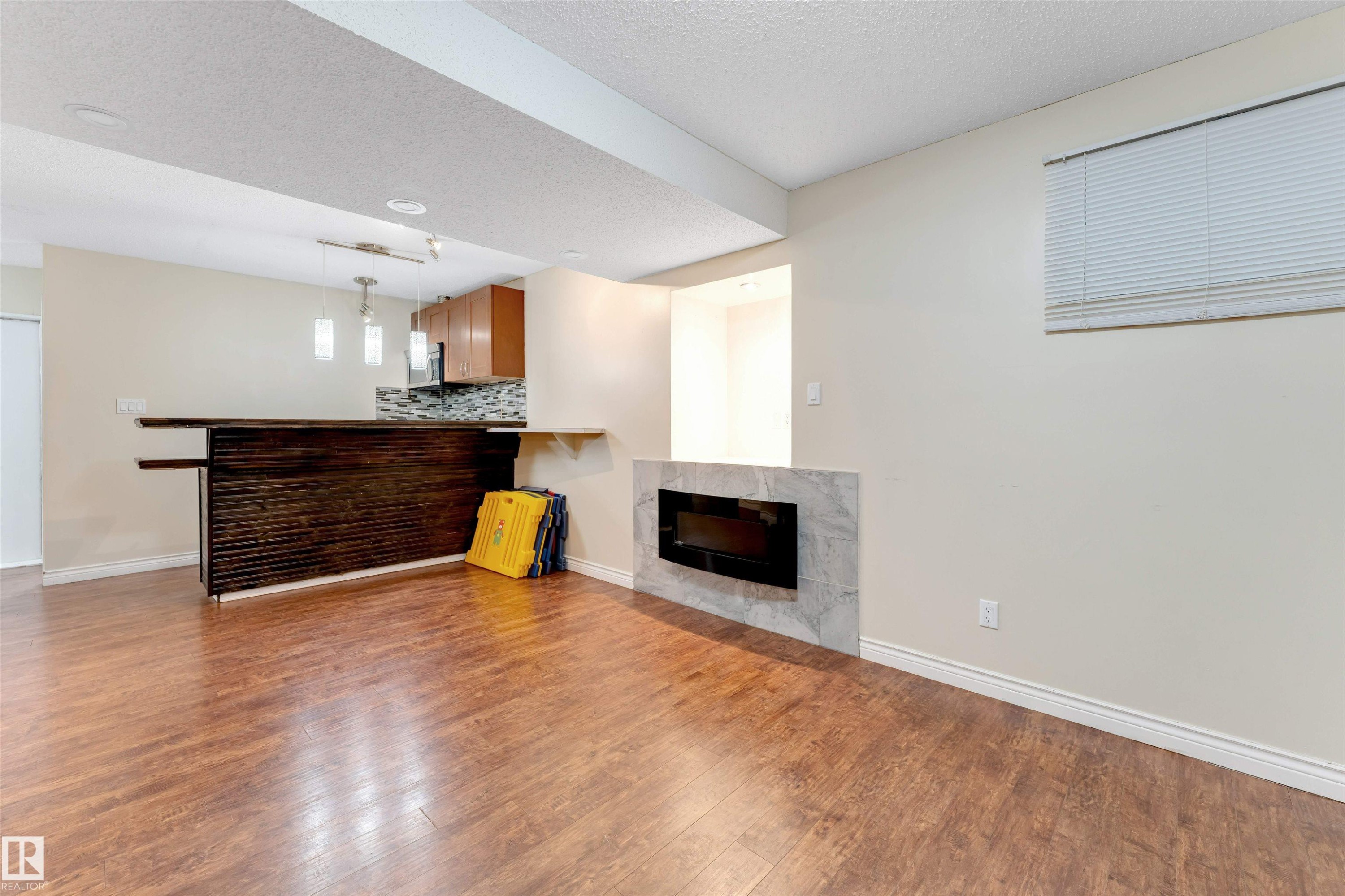 Unfurnished living room featuring a fireplace, dark wood-type flooring, a bar, and a textured ceiling - 18404 97A Avenue, Edmonton, AB - Indoor Photo Showing Other Room With Fireplace