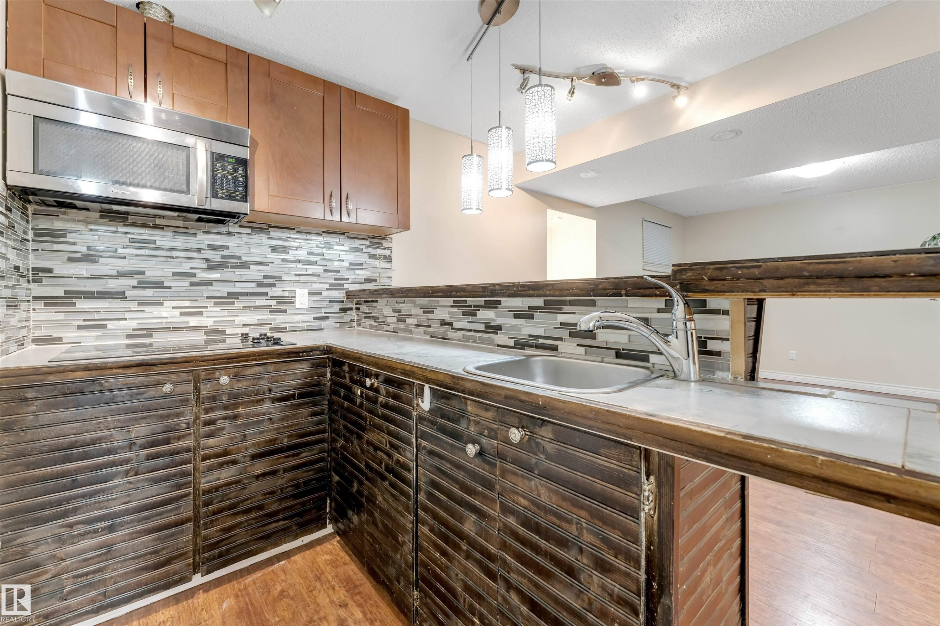Kitchen featuring stainless steel microwave, pendant lighting, light wood-style floors, tasteful backsplash, and brown cabinetry - 18404 97A Avenue, Edmonton, AB - Indoor Photo Showing Kitchen With Upgraded Kitchen