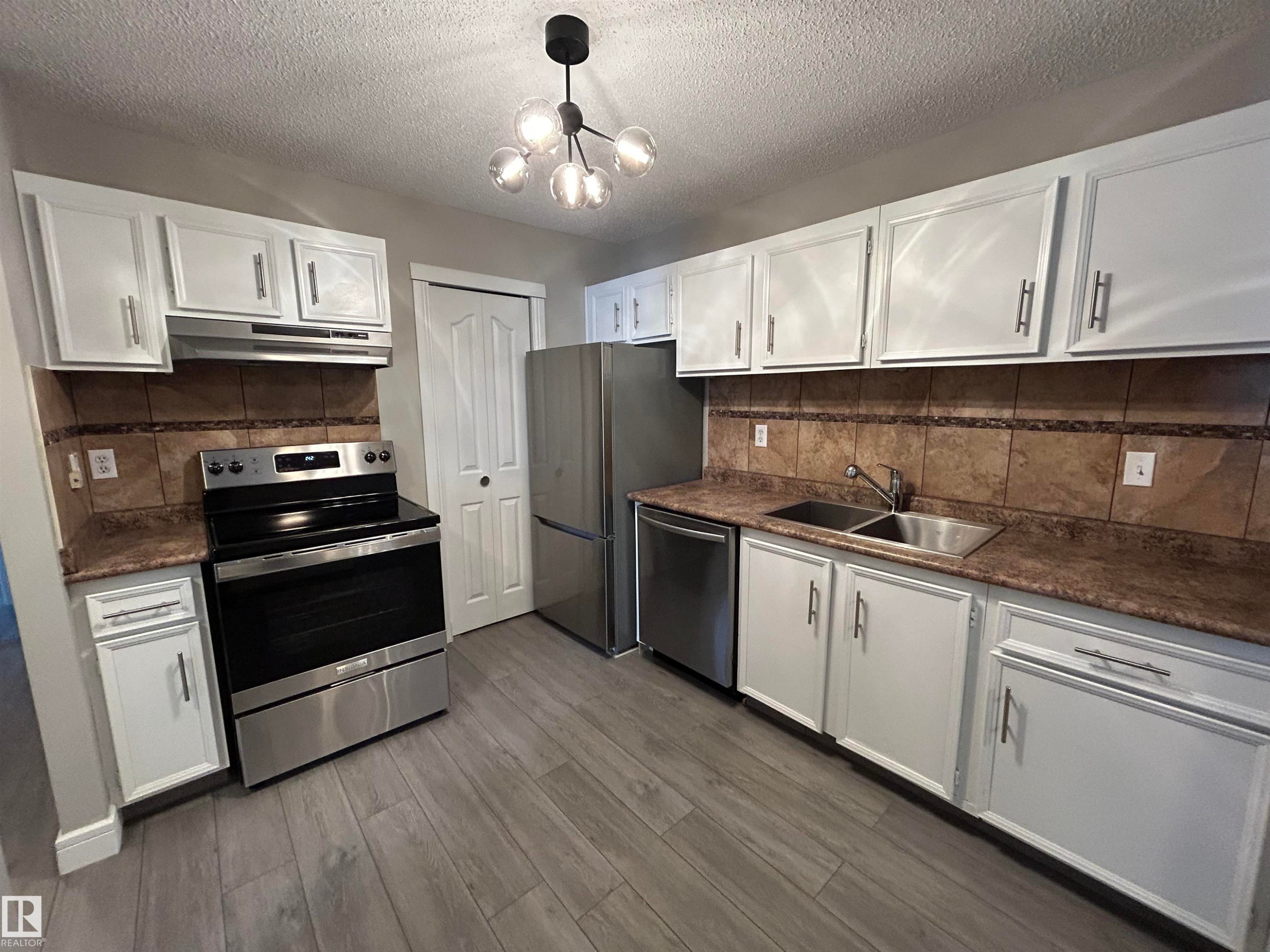 Kitchen with white cabinets, appliances with stainless steel finishes, backsplash, a textured ceiling, and decorative light fixtures - 53 14620 26 Street, Edmonton, AB - Indoor Photo Showing Kitchen With Double Sink