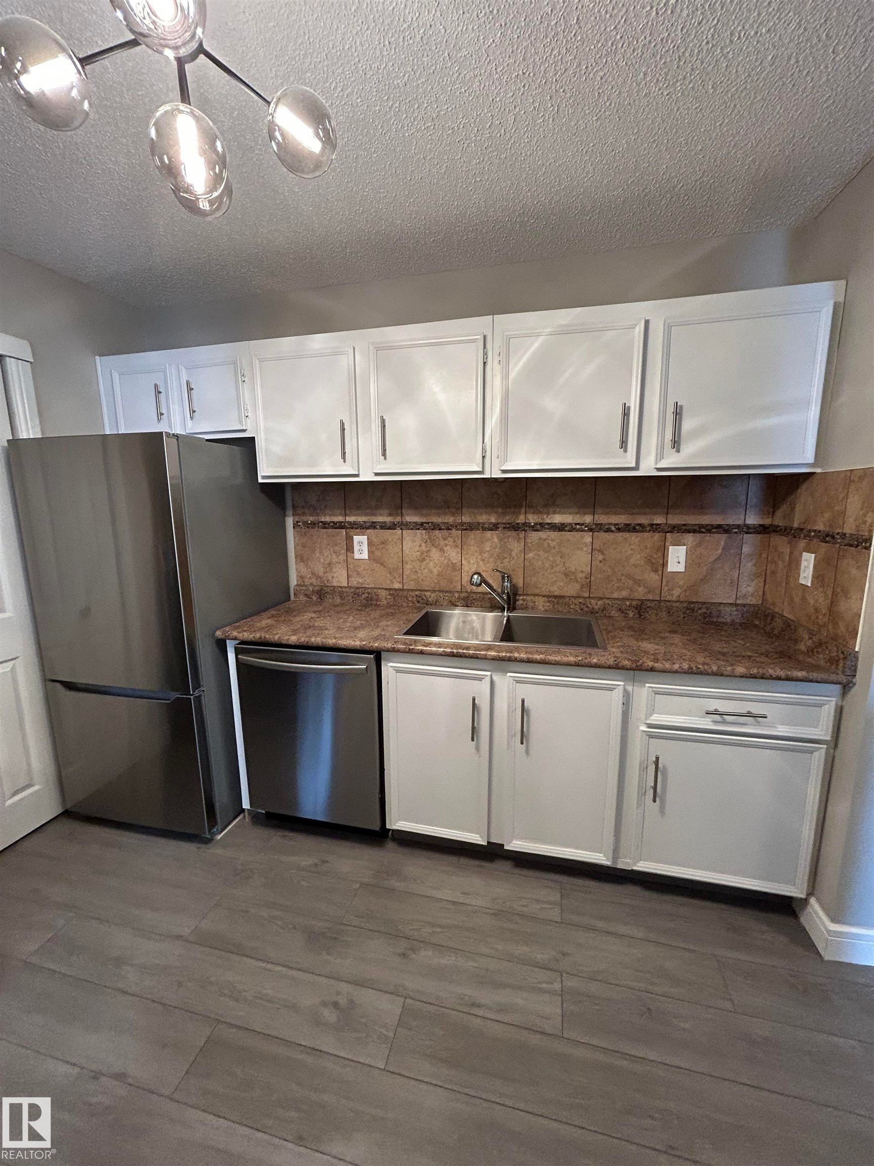 Kitchen with white cabinets, appliances with stainless steel finishes, a textured ceiling, tasteful backsplash, and dark wood finished floors - 53 14620 26 Street, Edmonton, AB - Indoor Photo Showing Kitchen With Double Sink