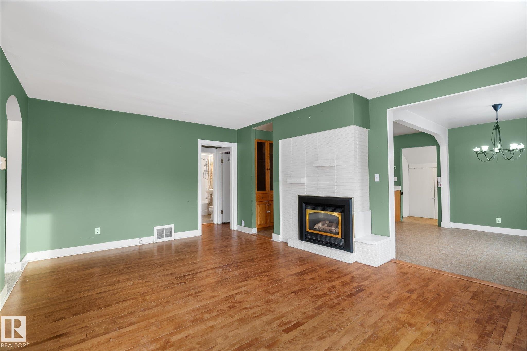 Unfurnished living room with arched walkways, a brick fireplace, wood finished floors, and a chandelier - 10429 143 Street, Edmonton, AB - Indoor Photo Showing Living Room With Fireplace
