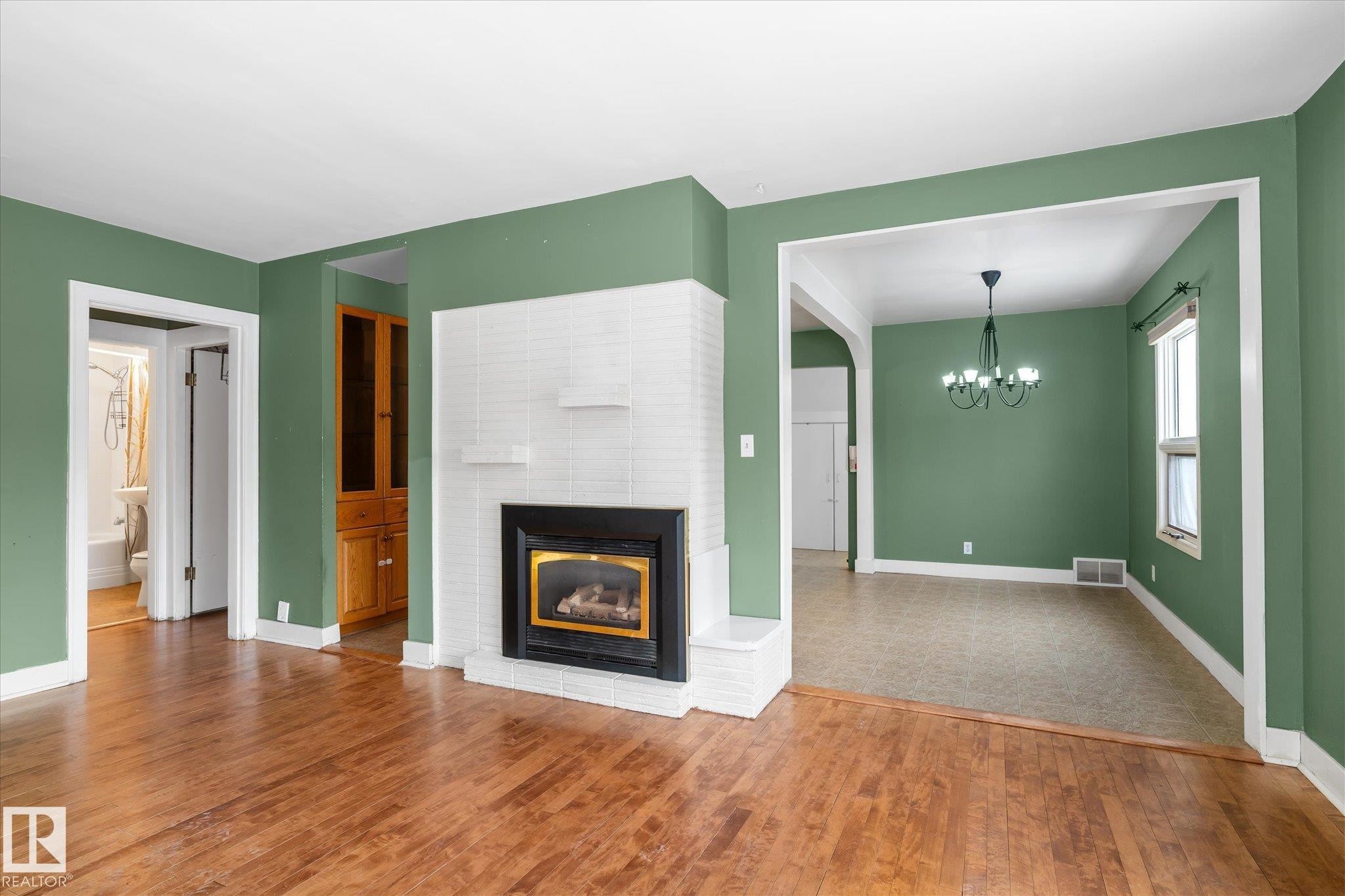 Unfurnished living room featuring a fireplace, a chandelier, and wood-type flooring - 10429 143 Street, Edmonton, AB - Indoor Photo Showing Living Room With Fireplace