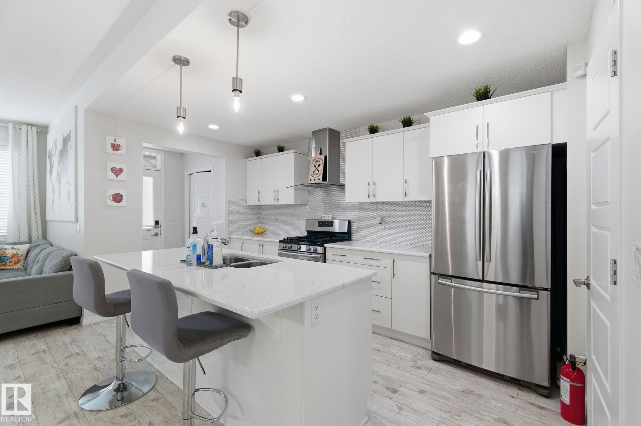 Kitchen with appliances with stainless steel finishes, a kitchen island with sink, tasteful backsplash, wall chimney range hood, and white cabinetry - 1511 Secord Rd, Edmonton, AB - Indoor Photo Showing Kitchen With Stainless Steel Kitchen With Double Sink With Upgraded Kitchen