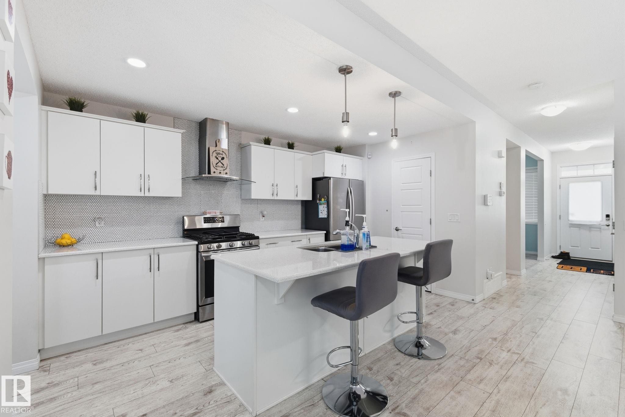 Kitchen featuring appliances with stainless steel finishes, white cabinets, wall chimney range hood, a kitchen breakfast bar, and hanging light fixtures - 1511 Secord Rd, Edmonton, AB - Indoor Photo Showing Kitchen With Stainless Steel Kitchen With Upgraded Kitchen