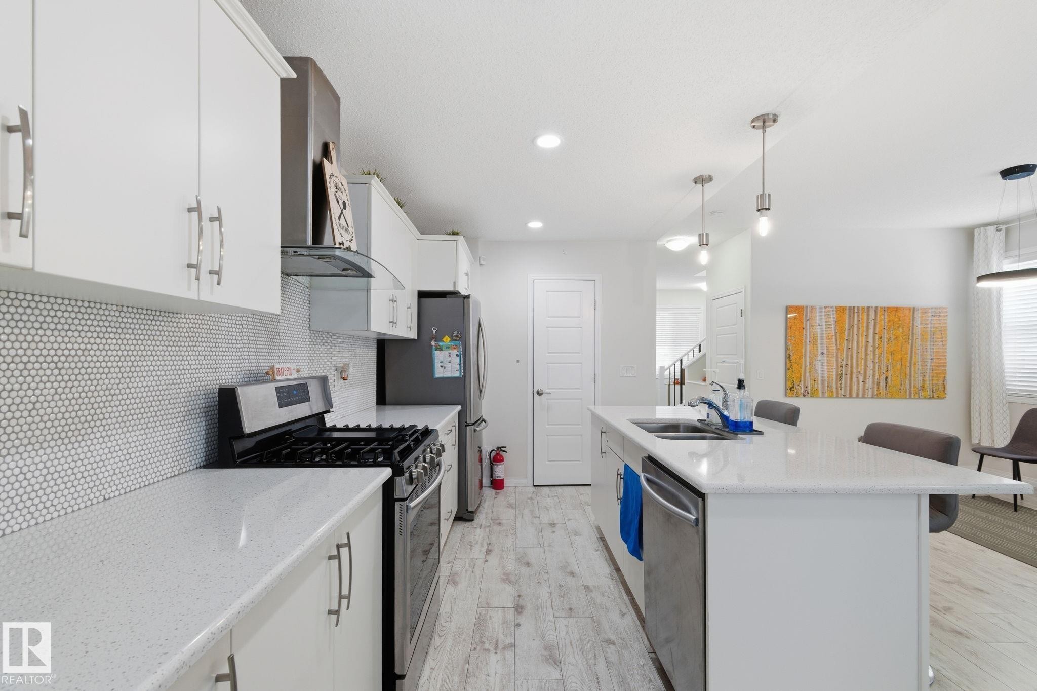 Kitchen featuring appliances with stainless steel finishes, a breakfast bar, white cabinets, light wood-type flooring, and pendant lighting - 1511 Secord Rd, Edmonton, AB - Indoor Photo Showing Kitchen With Double Sink With Upgraded Kitchen