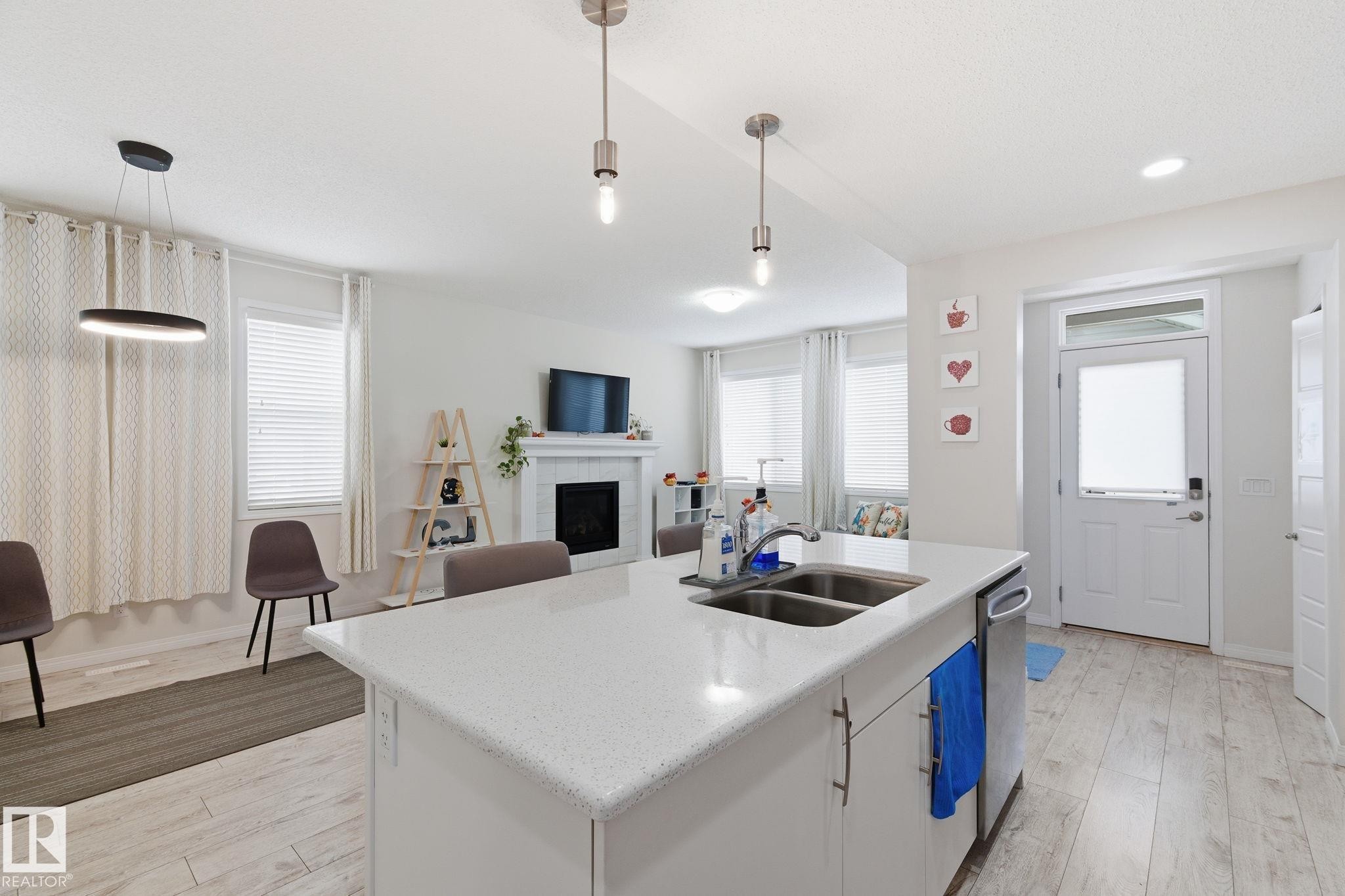 Kitchen with a fireplace, white cabinets, decorative light fixtures, light wood finished floors, and recessed lighting - 1511 Secord Rd, Edmonton, AB - Indoor Photo Showing Kitchen With Double Sink