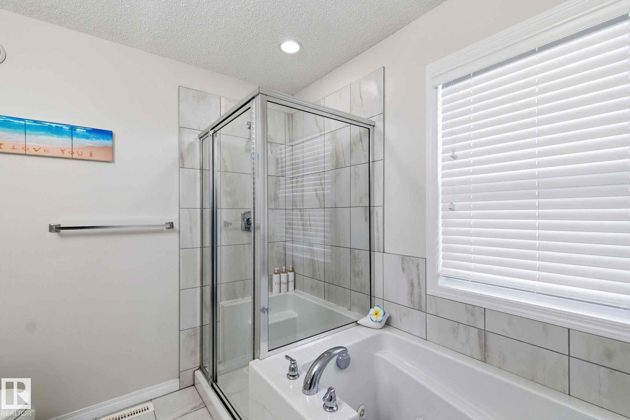 Full bath with a textured ceiling, a jetted tub, a stall shower, healthy amount of natural light, and tile patterned floors - 1511 Secord Rd, Edmonton, AB - Indoor Photo Showing Bathroom