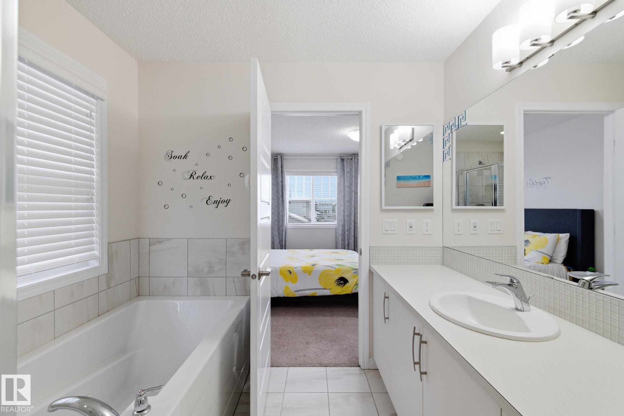 Ensuite bathroom featuring light tile patterned flooring, vanity, a bath, a textured ceiling, and light colored carpet - 1511 Secord Rd, Edmonton, AB - Indoor Photo Showing Bathroom
