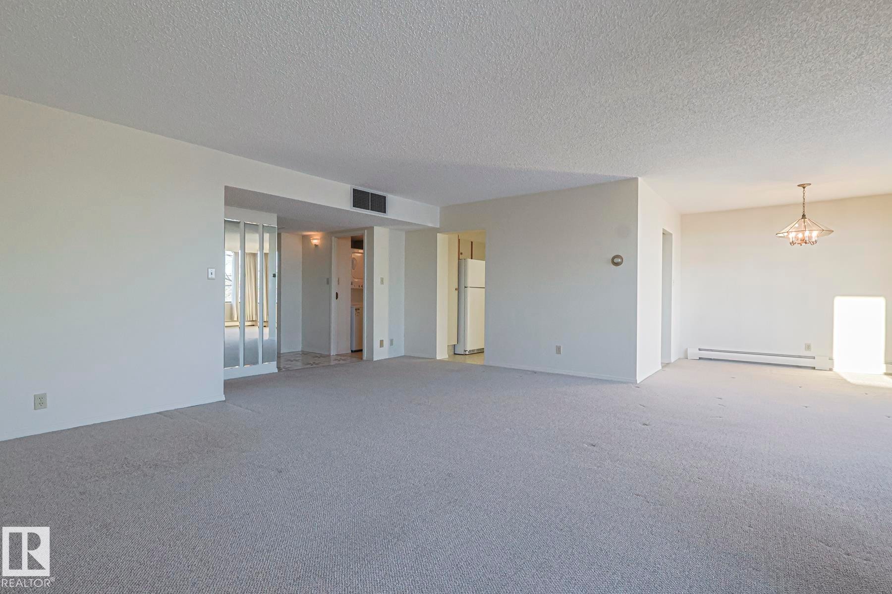Spare room with a textured ceiling, a chandelier, carpet flooring, and baseboard heating - 302 8340 Jasper Avenue Nw, Edmonton, AB - Indoor Photo Showing Other Room