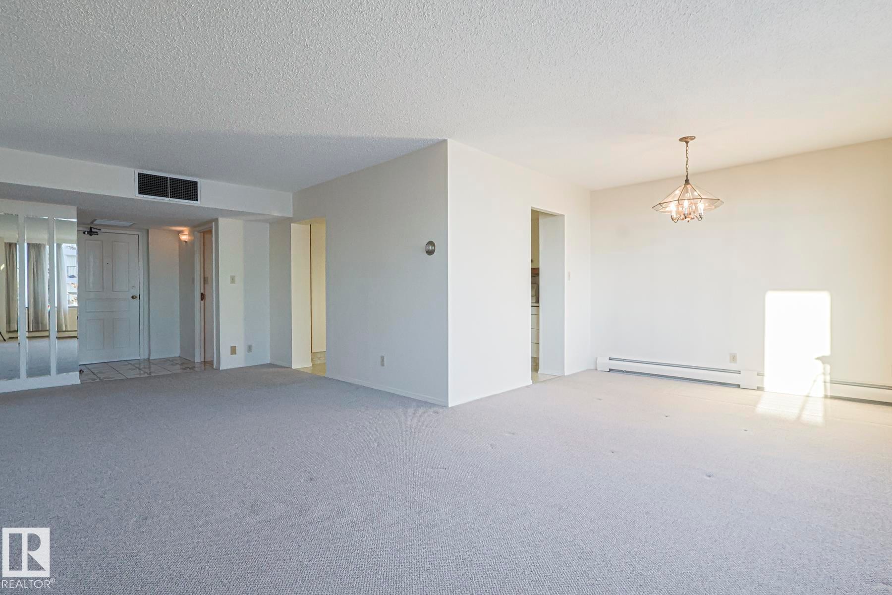 Carpeted empty room featuring a textured ceiling, a chandelier, and baseboard heating - 302 8340 Jasper Avenue Nw, Edmonton, AB - Indoor Photo Showing Other Room