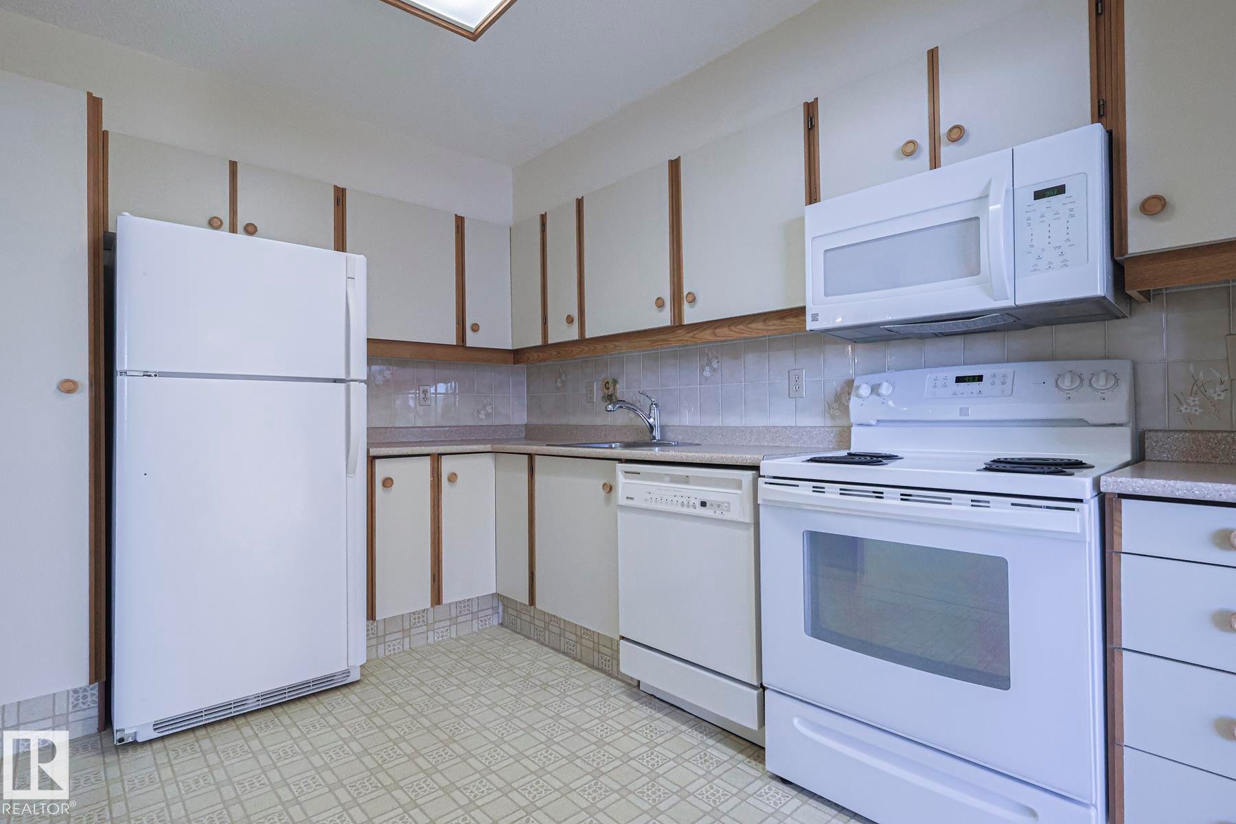 Kitchen with white appliances, light flooring, white cabinetry, light countertops, and backsplash - 302 8340 Jasper Avenue Nw, Edmonton, AB - Indoor Photo Showing Kitchen