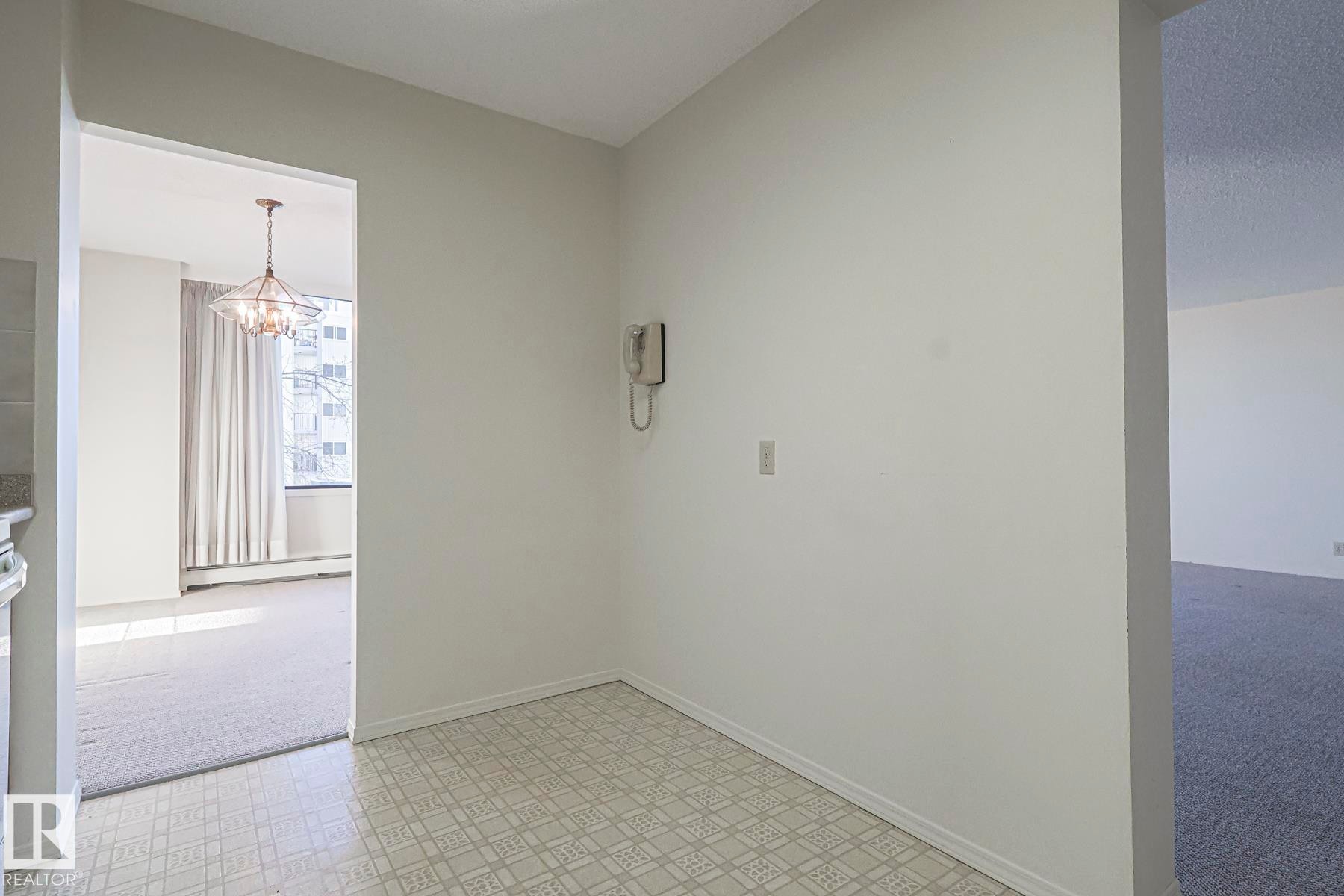 Empty room featuring light flooring, a chandelier, a baseboard radiator, and light colored carpet - 302 8340 Jasper Avenue Nw, Edmonton, AB - Indoor Photo Showing Other Room