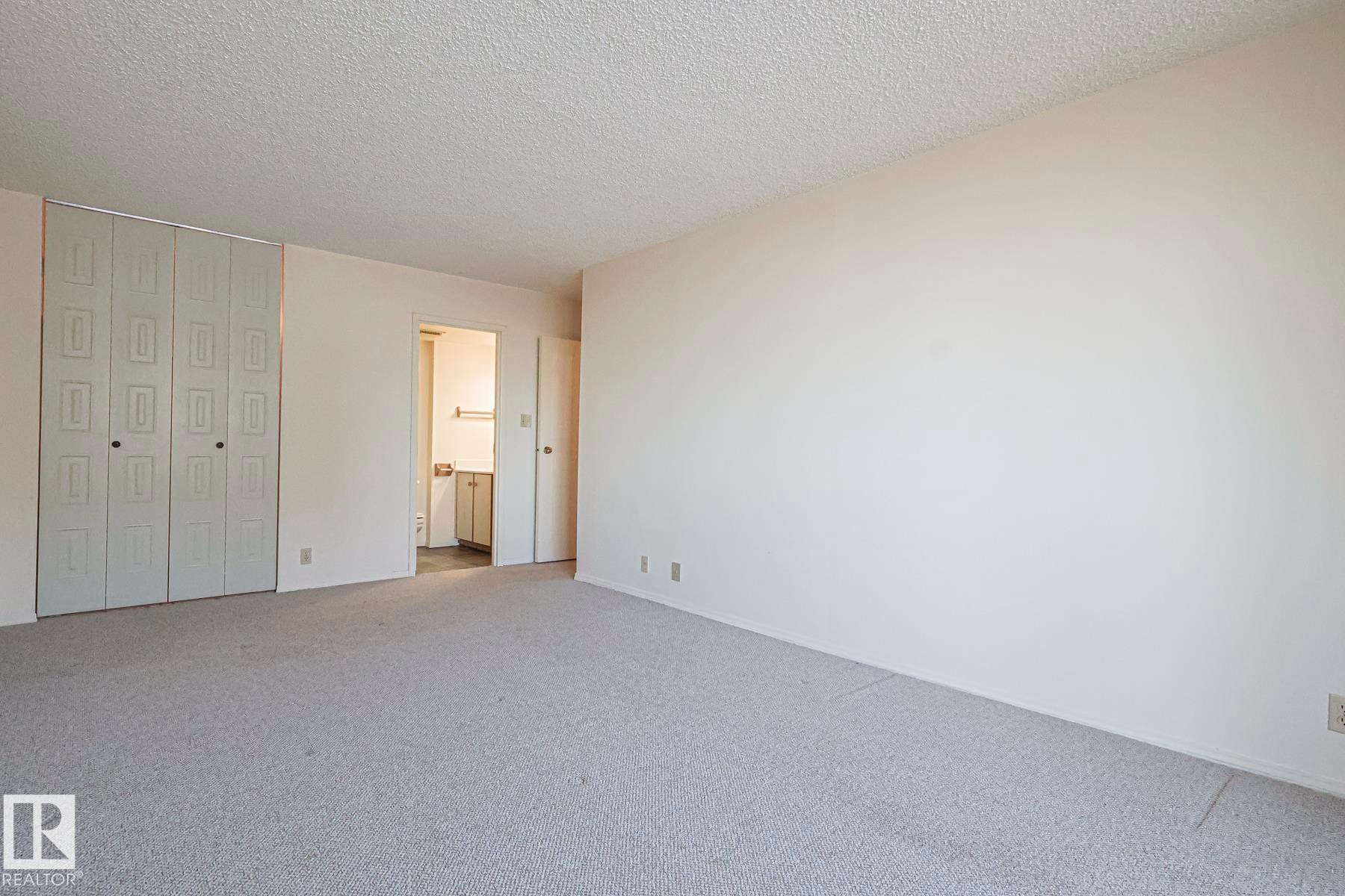 Unfurnished bedroom with a textured ceiling, a closet, carpet, and connected bathroom - 302 8340 Jasper Avenue Nw, Edmonton, AB - Indoor Photo Showing Other Room