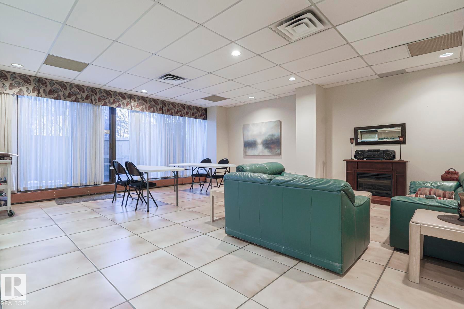 Living room with a paneled ceiling, light tile patterned floors, and a fireplace - 302 8340 Jasper Avenue Nw, Edmonton, AB - Indoor Photo Showing Other Room