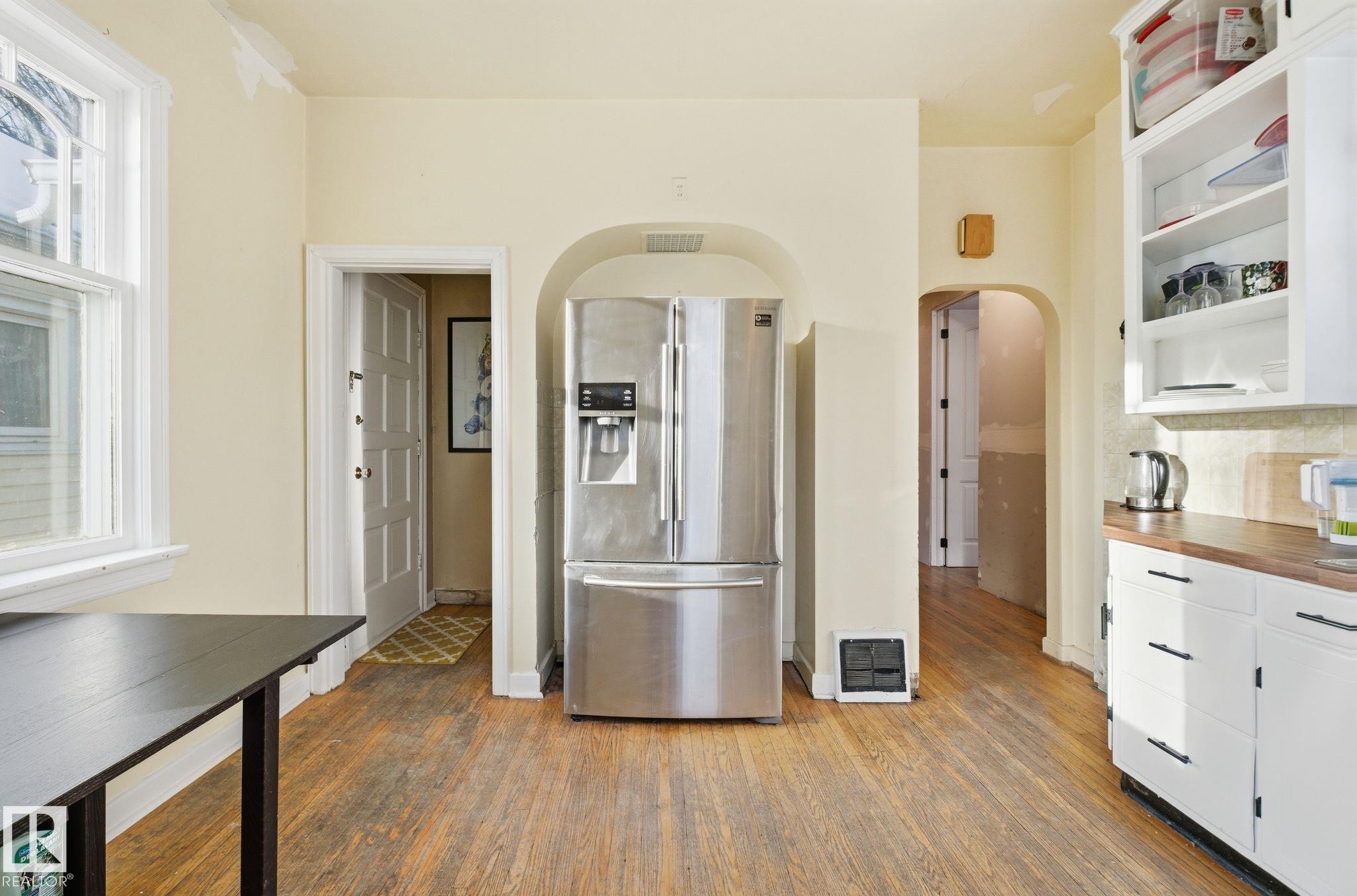 Kitchen featuring stainless steel refrigerator with ice dispenser, white cabinets, dark wood-style flooring, and arched walkways - 11515 101 Street, Edmonton, AB - Indoor Photo Showing Kitchen