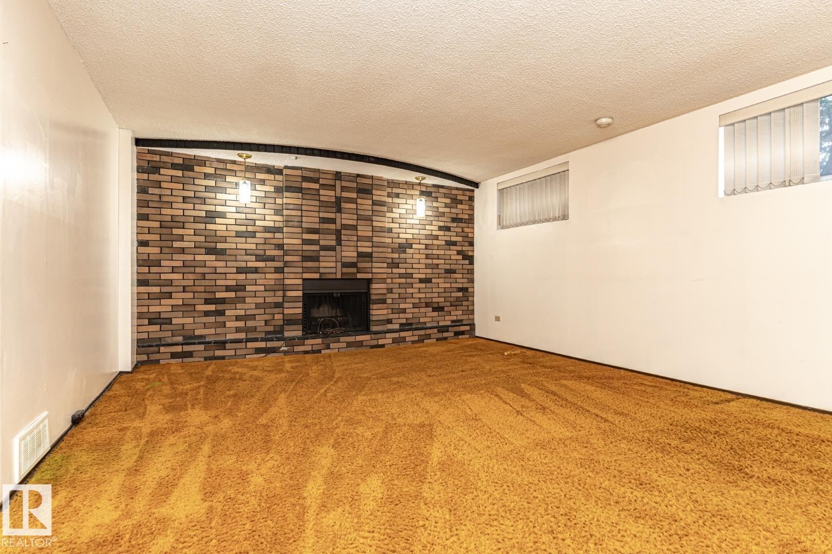 Unfurnished living room with a textured ceiling, carpet floors, a fireplace, lofted ceiling, and brick wall - 10207 165 Avenue, Edmonton, AB - Indoor With Fireplace