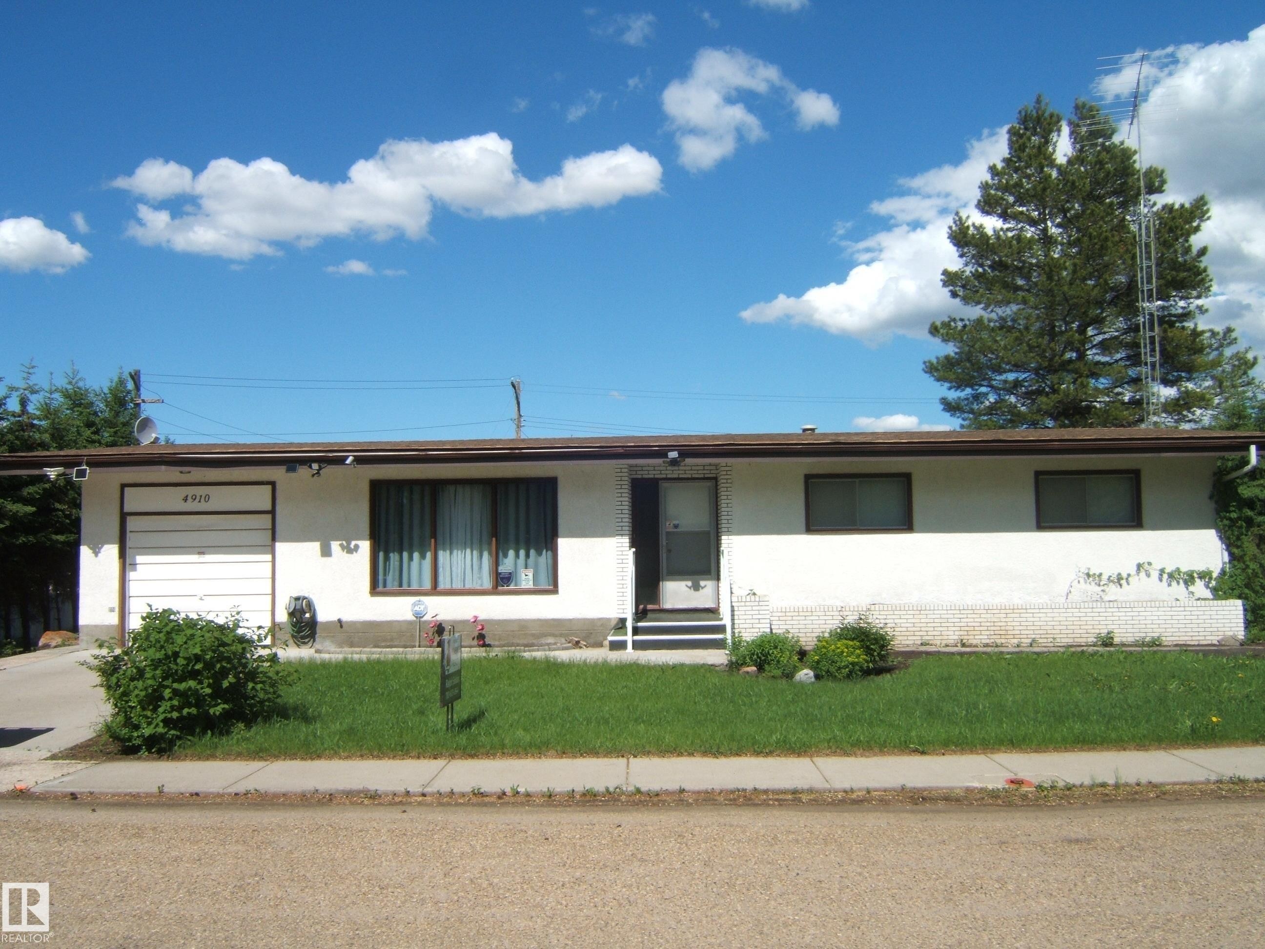 Single-story residence featuring a white stucco exterior with a brown fascia, an attached single-car garage, and a front entry door with exterior steps - 4910 53 Avenue, Willingdon, AB