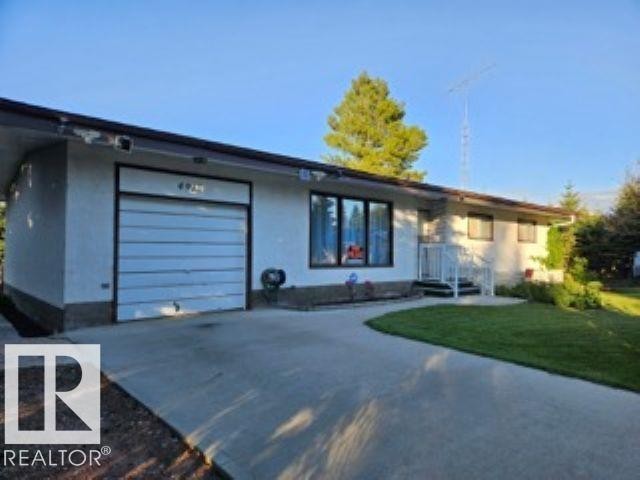 View of front of house with concrete driveway, stucco siding, a front lawn, and a garage - 4910 53 Avenue, Willingdon, AB