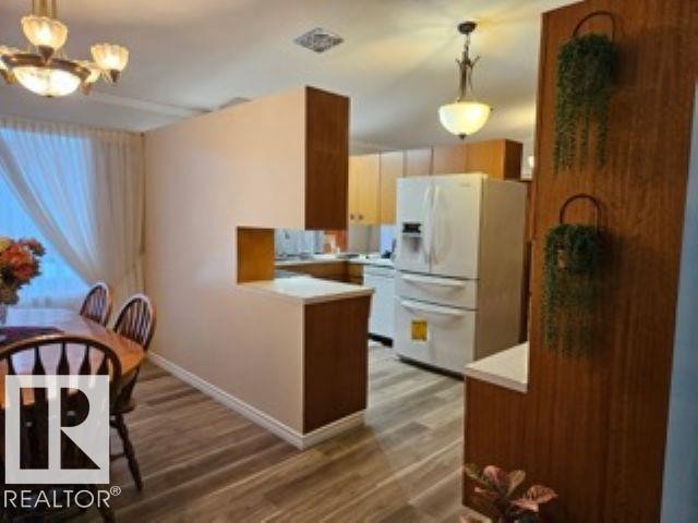Kitchen with white appliances, a peninsula, light countertops, pendant lighting, and light wood-style floors - 4910 53 Avenue, Willingdon, AB