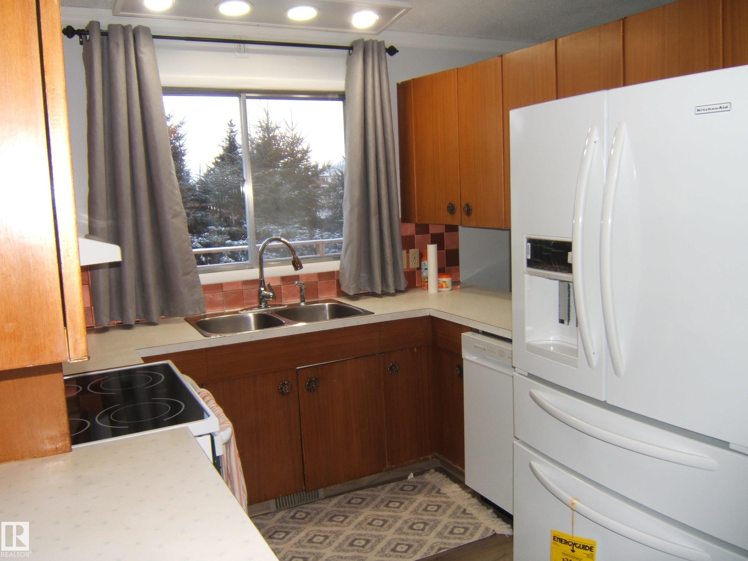 Kitchen featuring white appliances, light countertops, brown cabinets, backsplash, and extractor fan - 4910 53 Avenue, Willingdon, AB