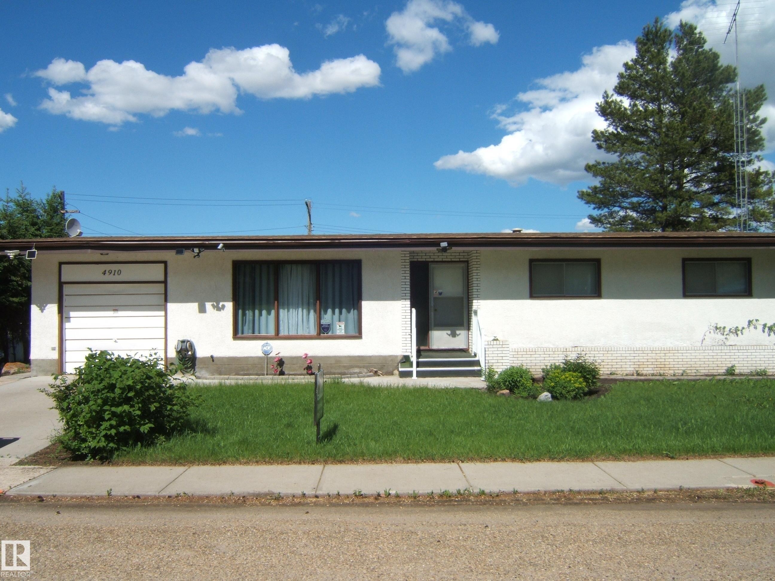 Single-story residence featuring a white exterior, attached single-car garage, and a front yard with established landscaping - 4910 53 Avenue, Willingdon, AB