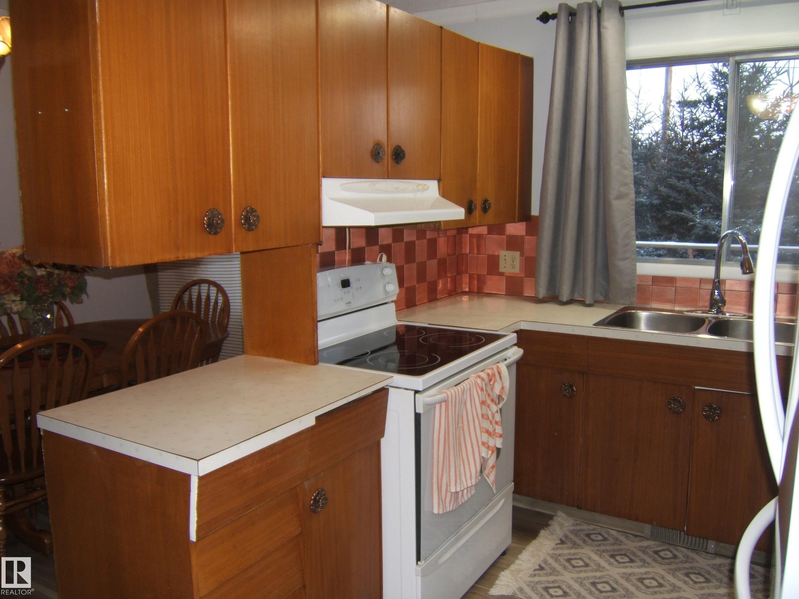 Kitchen featuring electric stove, under cabinet range hood, light countertops, stainless steel fridge, and brown cabinets - 4910 53 Avenue, Willingdon, AB