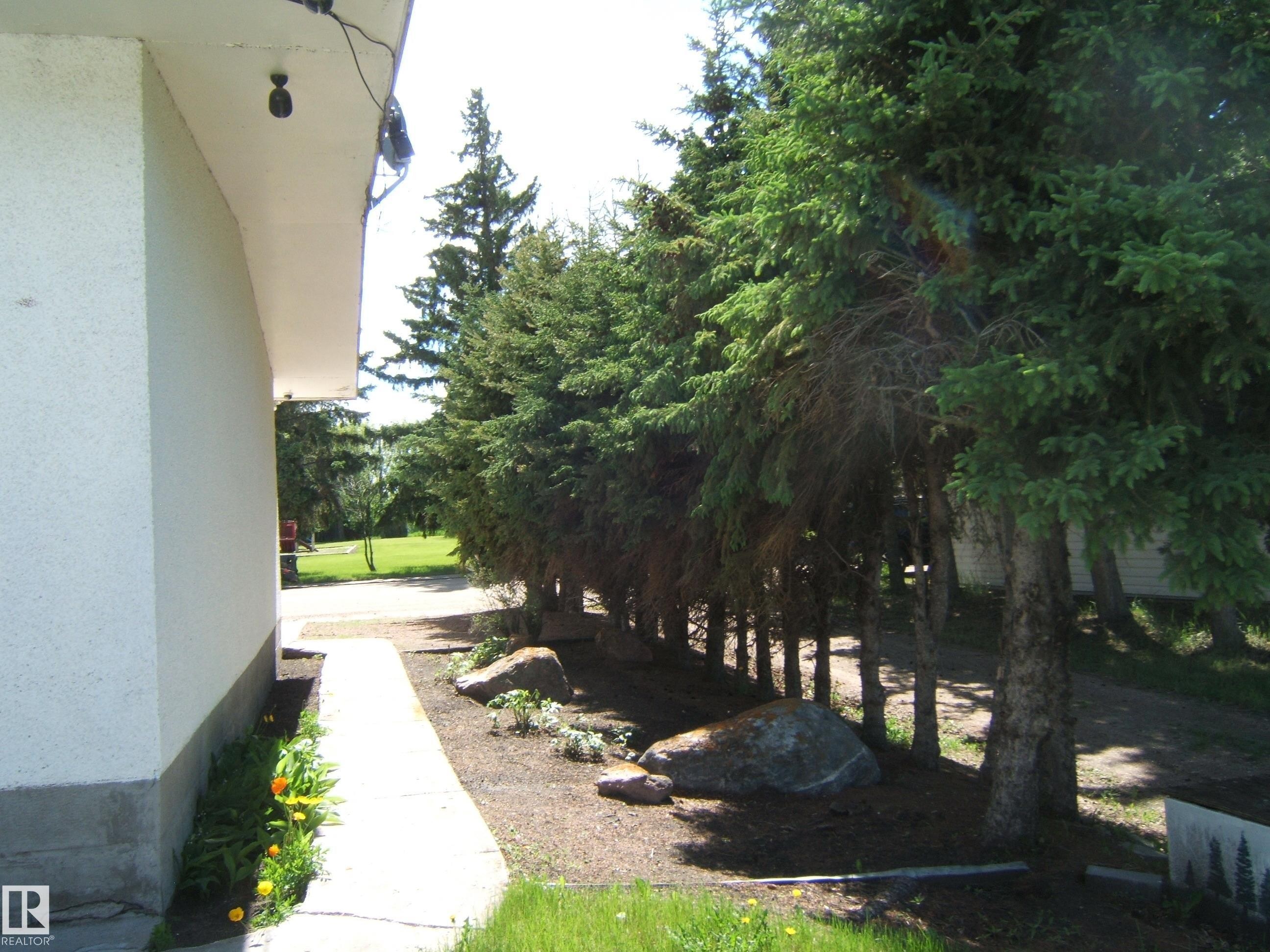 Exterior pathway featuring a concrete walkway, established evergreen trees, and decorative boulders - 4910 53 Avenue, Willingdon, AB